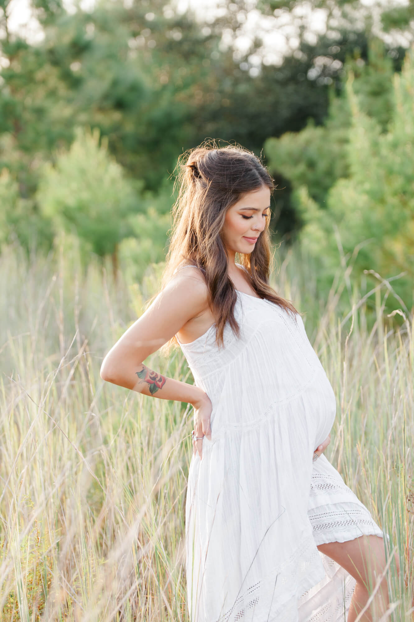 Beautiful mom stands in tall grass holding her pregnant belly for her maternity photos