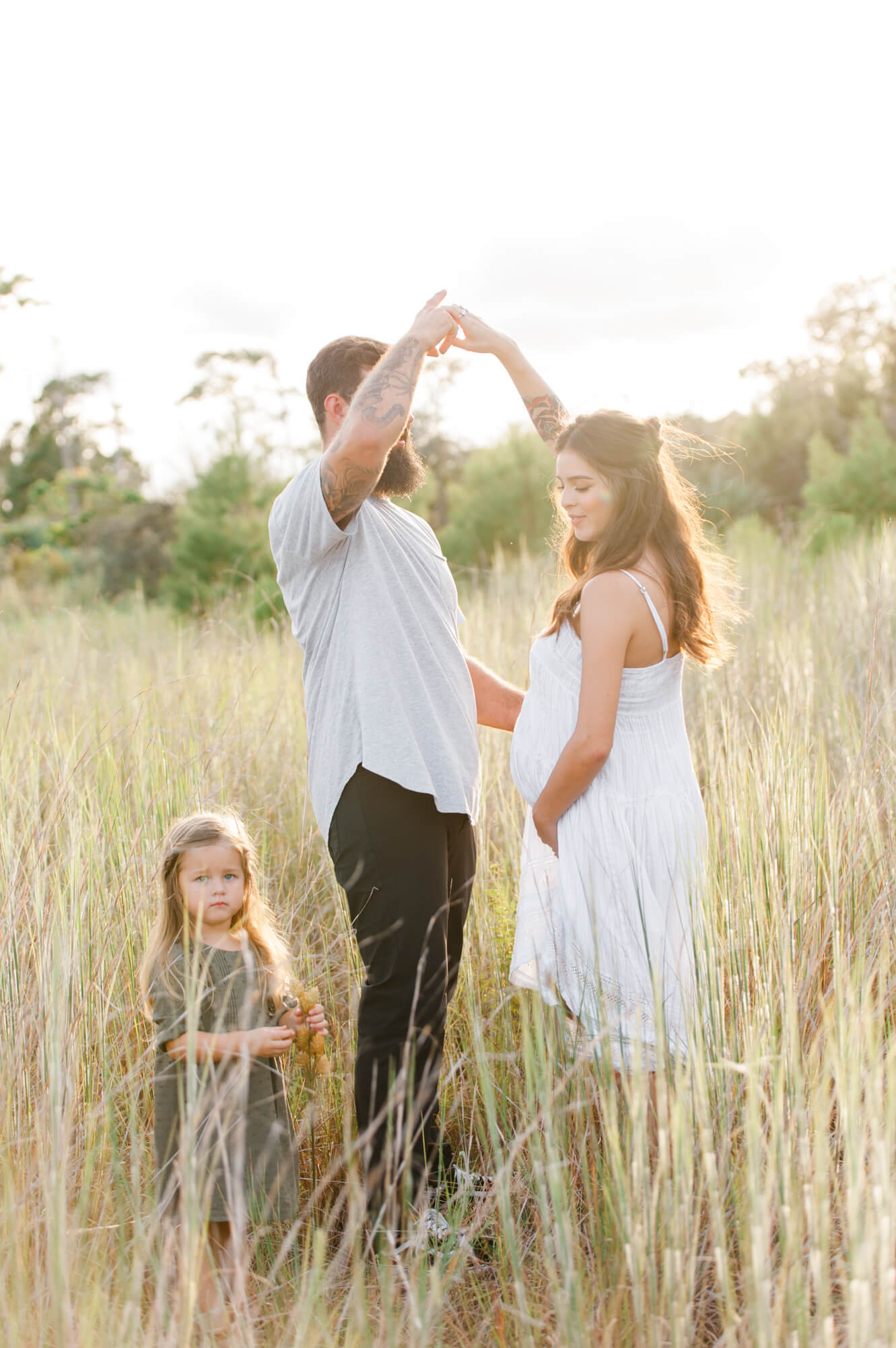 Family stands in tall grass field dancing while husband twirls wife during their maternity photos Heart 2 heart birth center
