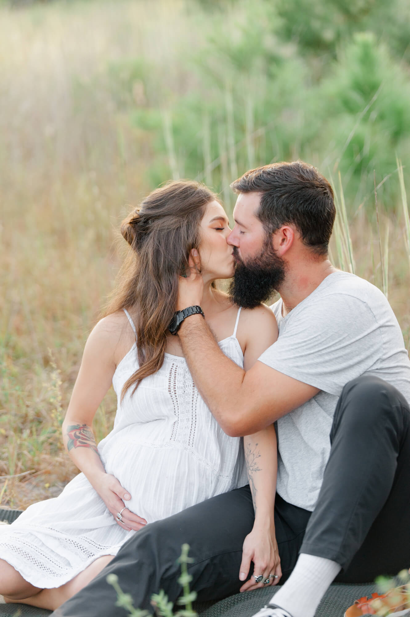 Pregnant wife kissing husband while sitting in a tall grass field in Orlando Heart 2 heart birth center