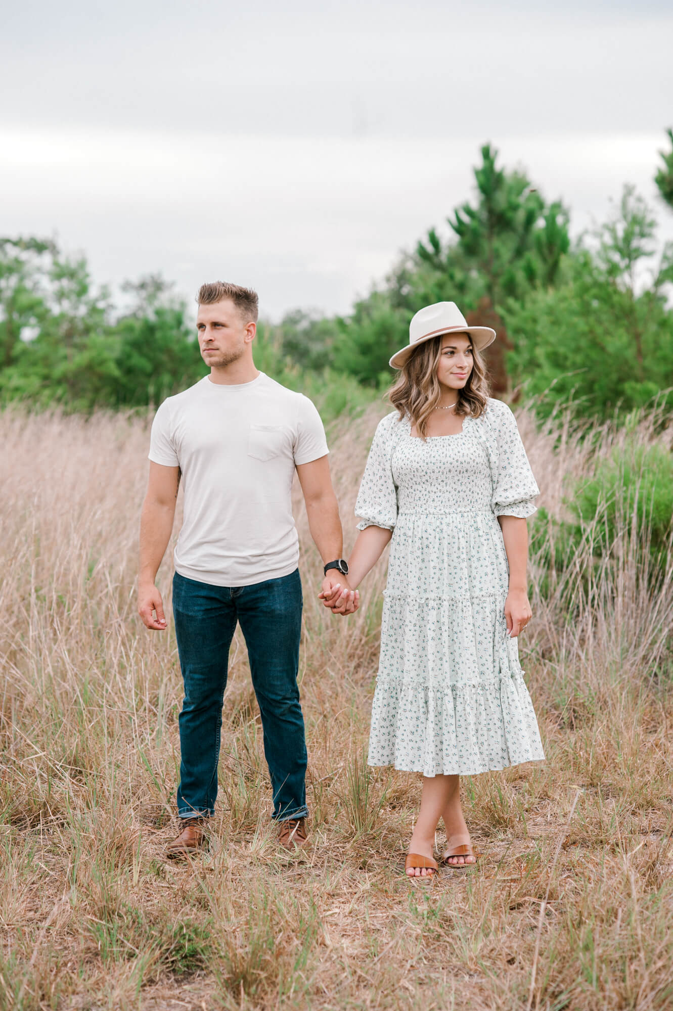 Husband + Wife standing in a field looking in separate directions while holding hands. 