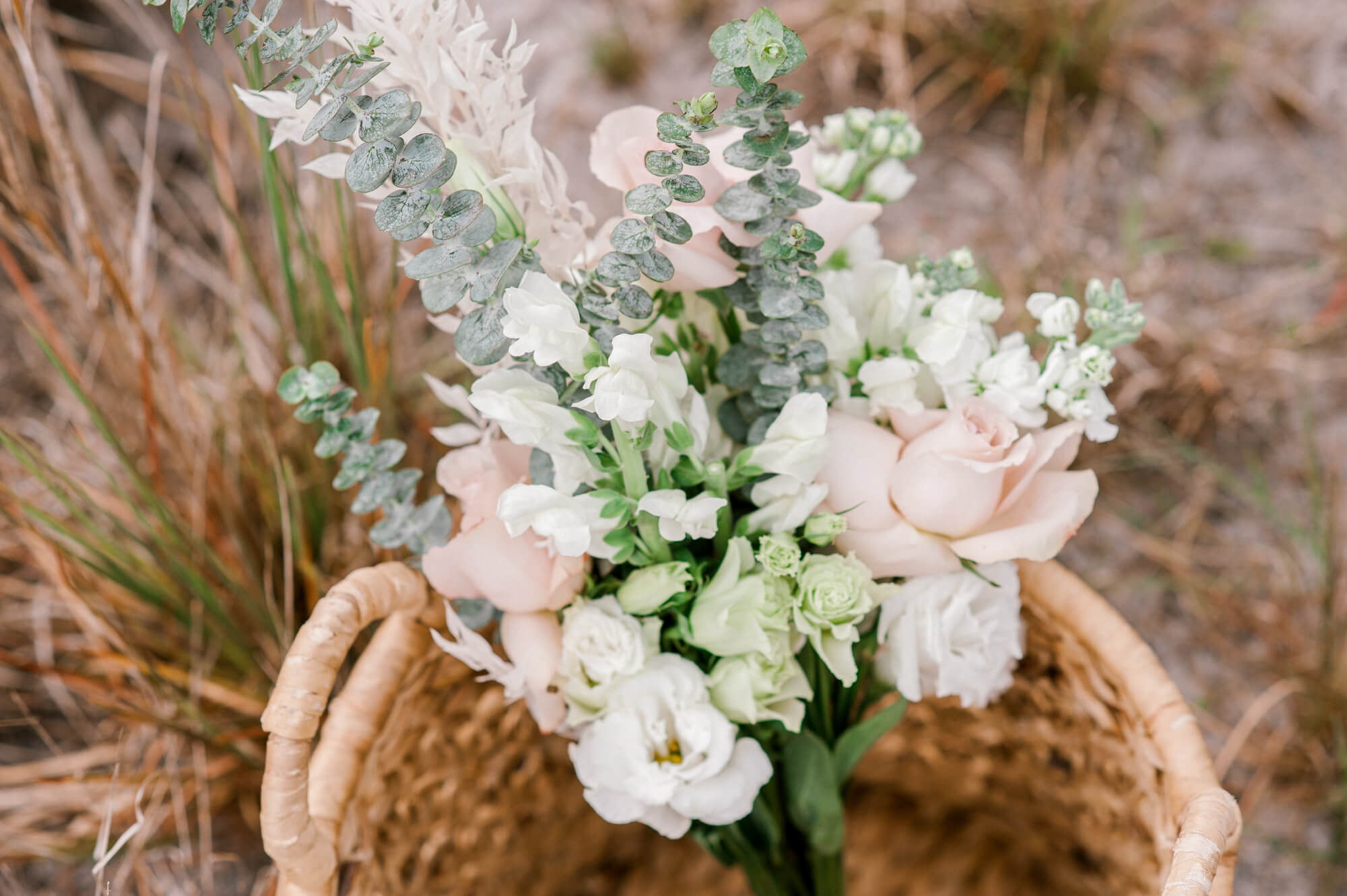A bouquet of florals in a wicker basket in the middle of a tall grass field.