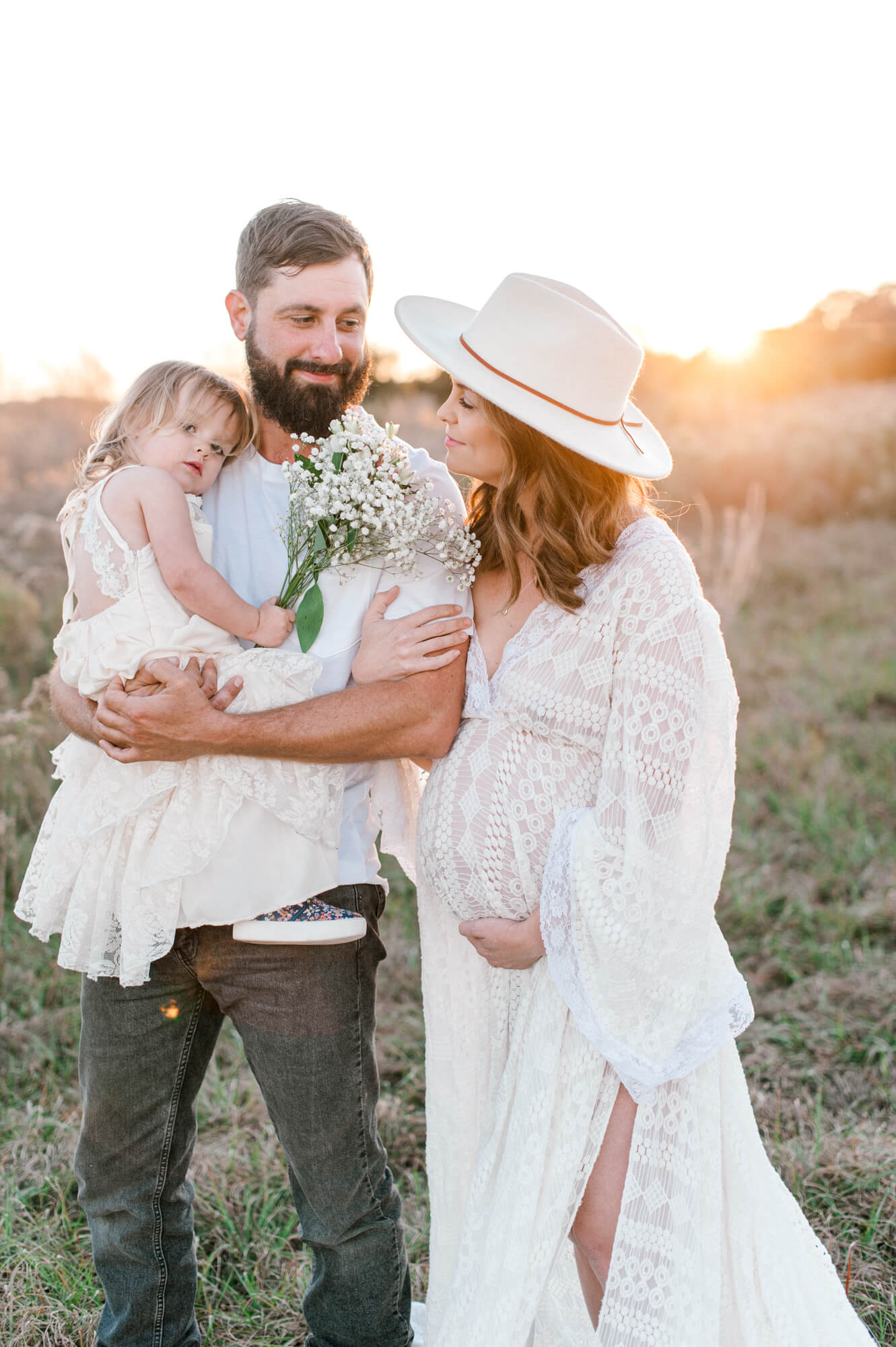 Closeup portrait of soon to be mom and dad holding daughter in a field. 