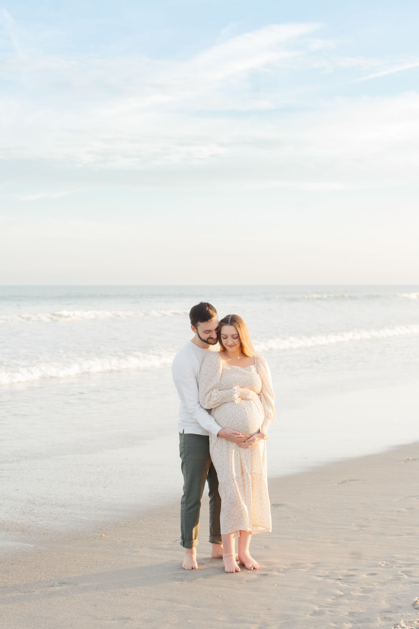 Expectant parents stand near the shoreline on Cocoa Beach and hold moms belly while looking down at their soon to be little girl!