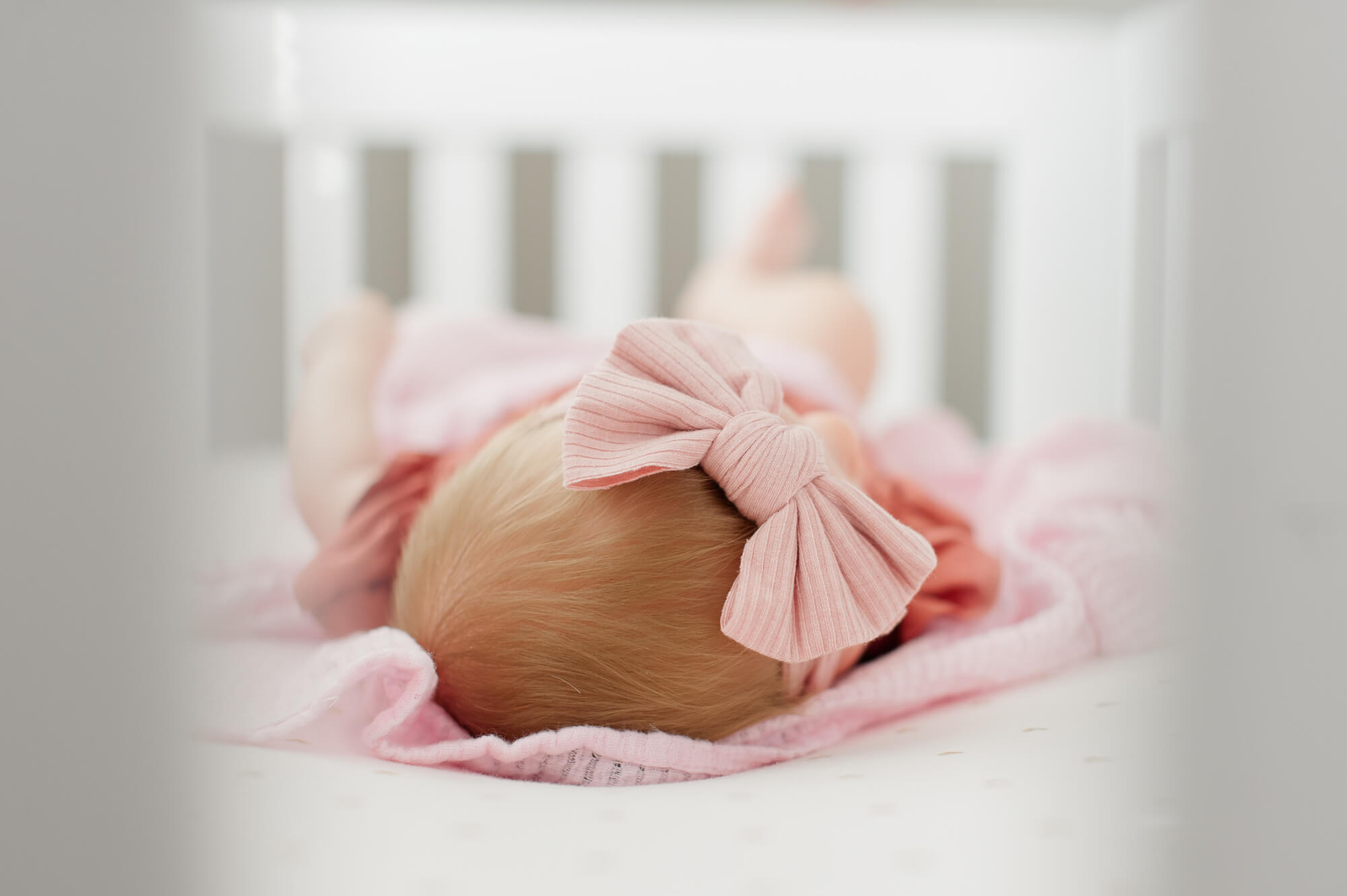 Closeup of newborn babygirls hair and pink bow through the crib railing.
