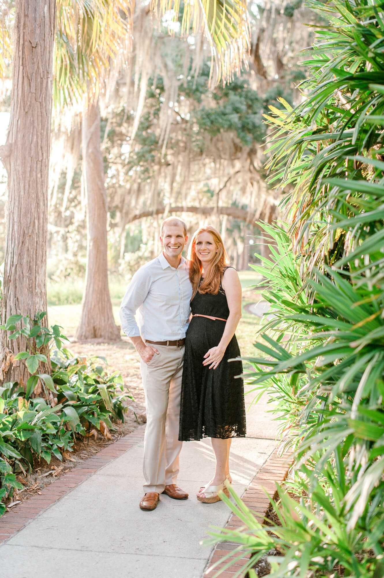 Mom and dad pose together holding belly on a path in the park. Baby boutiques in Orlando would be a great stop after their maternity photoshoot.