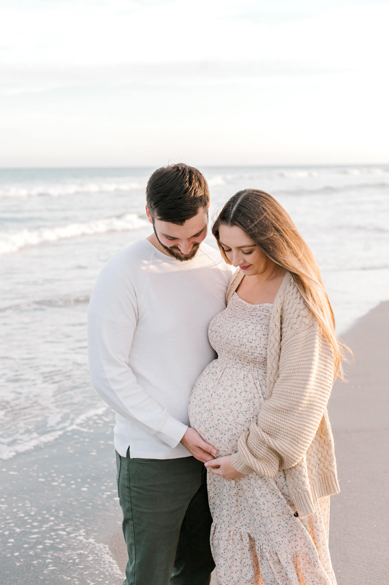 Soon to be parents of a babygirl admire and hold the moms belly on the beach while chatting about Tree of Life Birth Center.