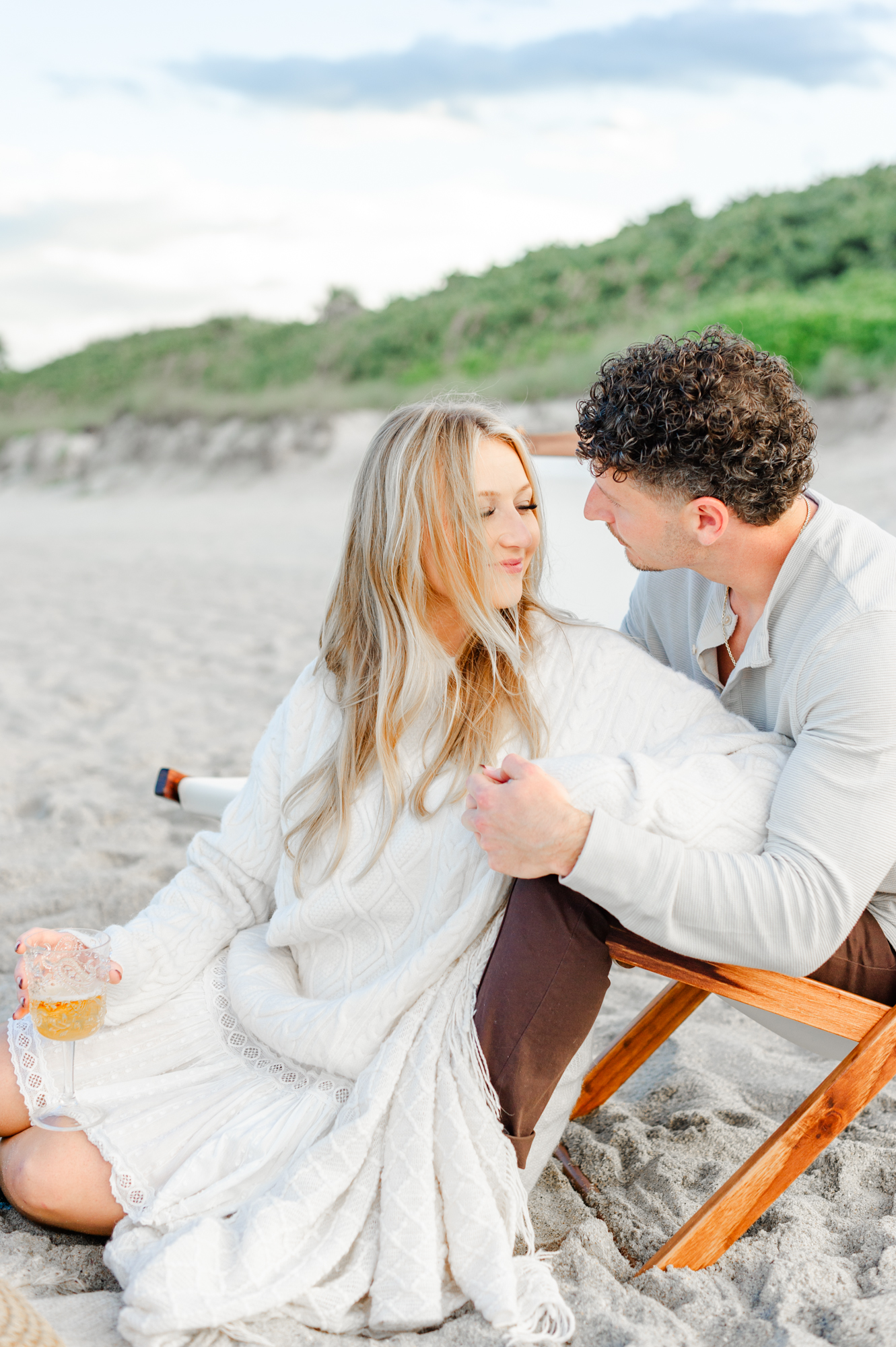 Couple flirts while cozied up on the beach for their luxury picnic date night.