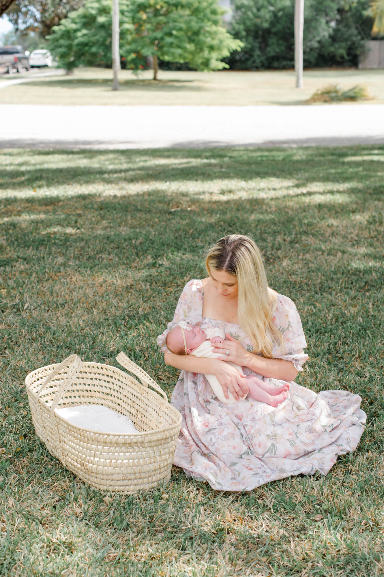 Sweet new mom wearing a floral dress from the client closet holding her newborn baby underneath an oak tree.