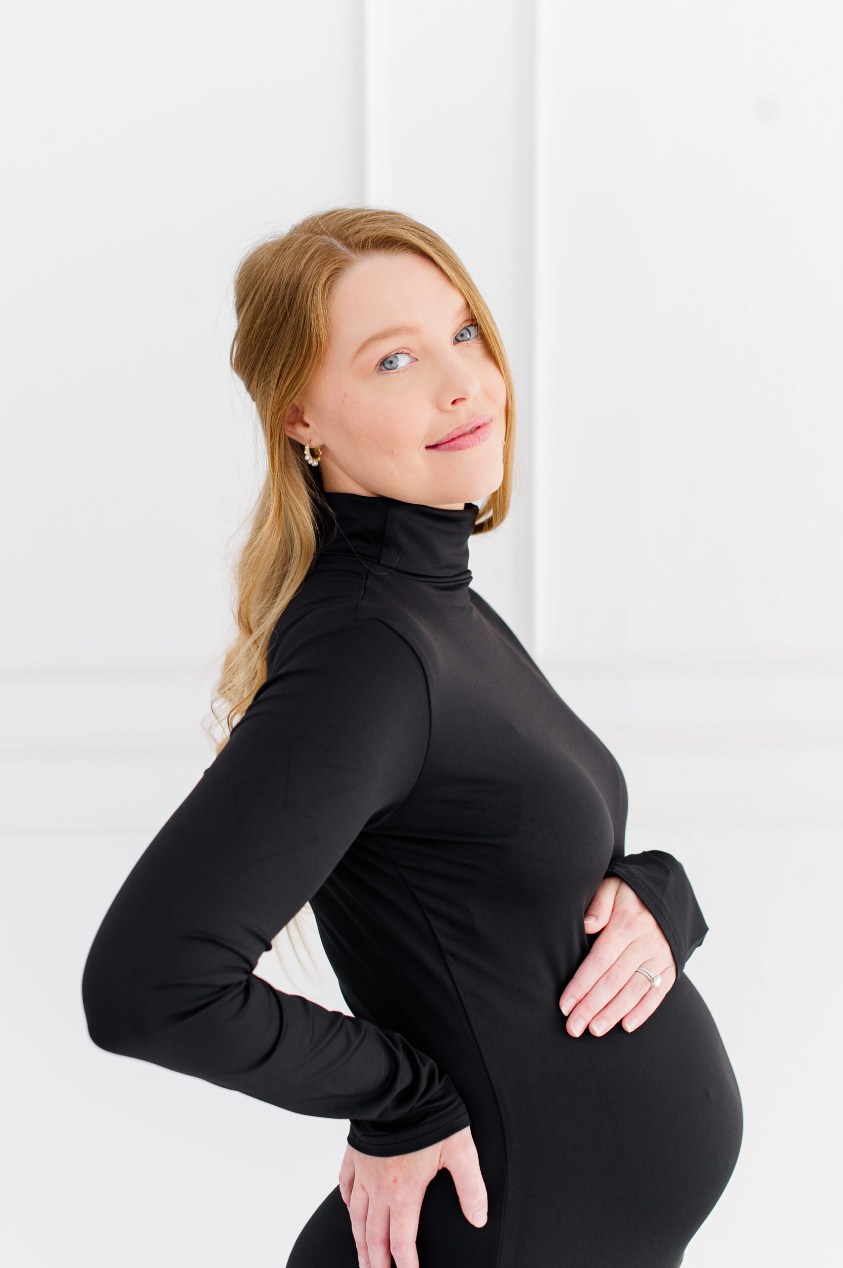 Pregnant mom holds her belly and stares straight into the camera wearing all black Sacred Birth Midwifery