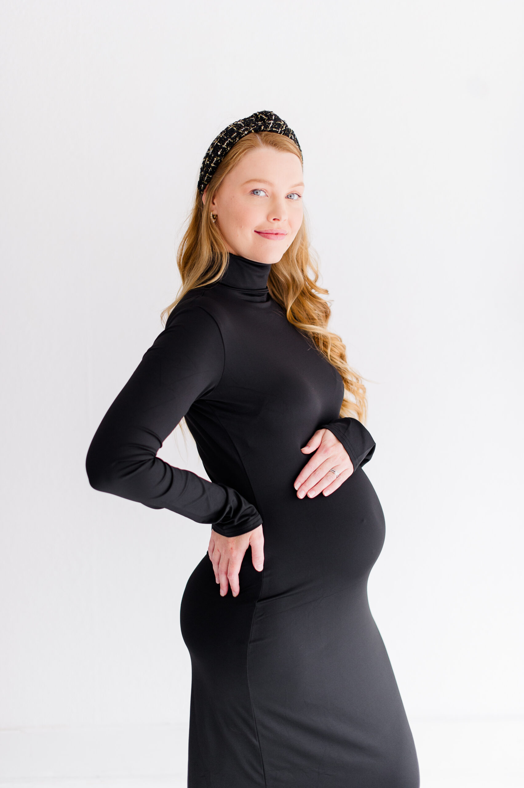 Stunning new mom holding her belly wearing all black longsleeve dress posing in a natural light studio in Orlando for her 20 week maternity photos.