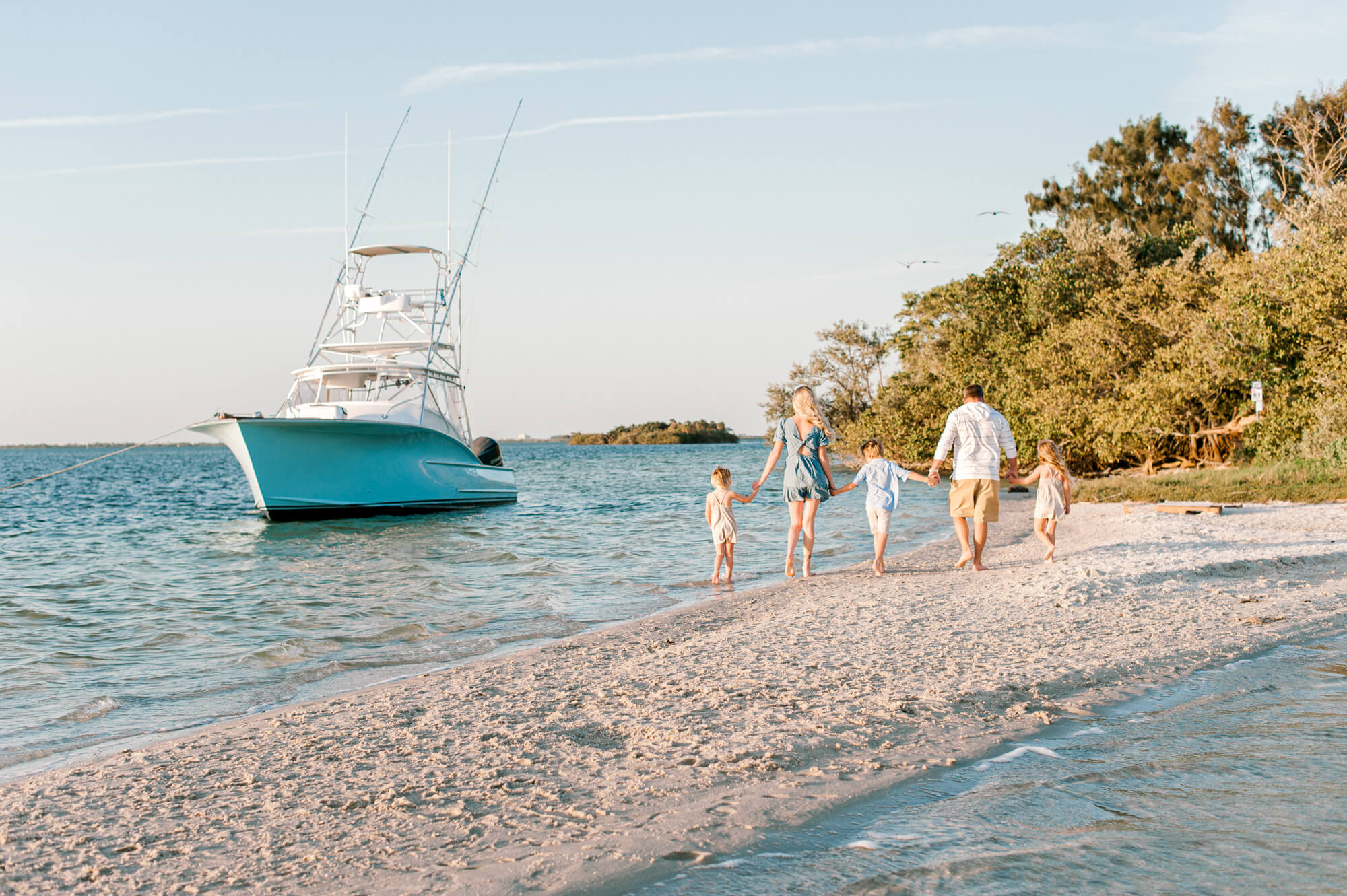 Family of five walk on Bird Island in Merritt Island, Florida toward their boat in the background holding hands at sunset.