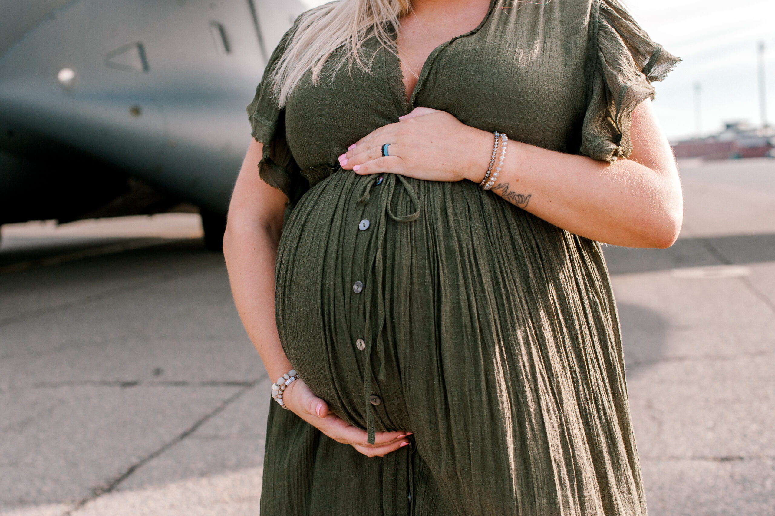 Close up of mom holding her pregnant belly with both hands on the Air Force Base flight line while thinking of hibiscus women's center.
