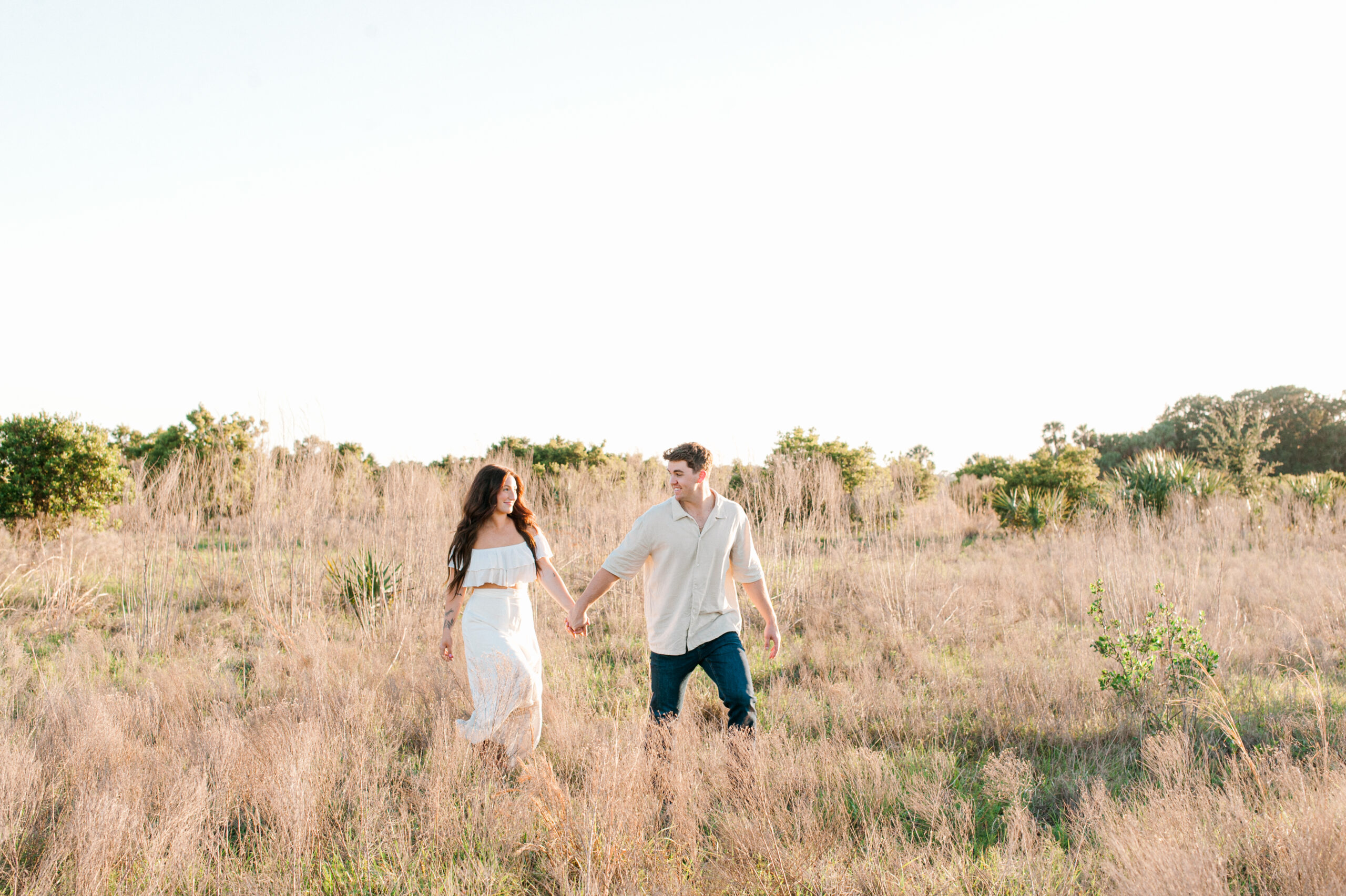 Beautiful image of a couples holding hands walking through a field of tall grass chatting about Project 7 Yoga in Downtown Orlando, Florida. 