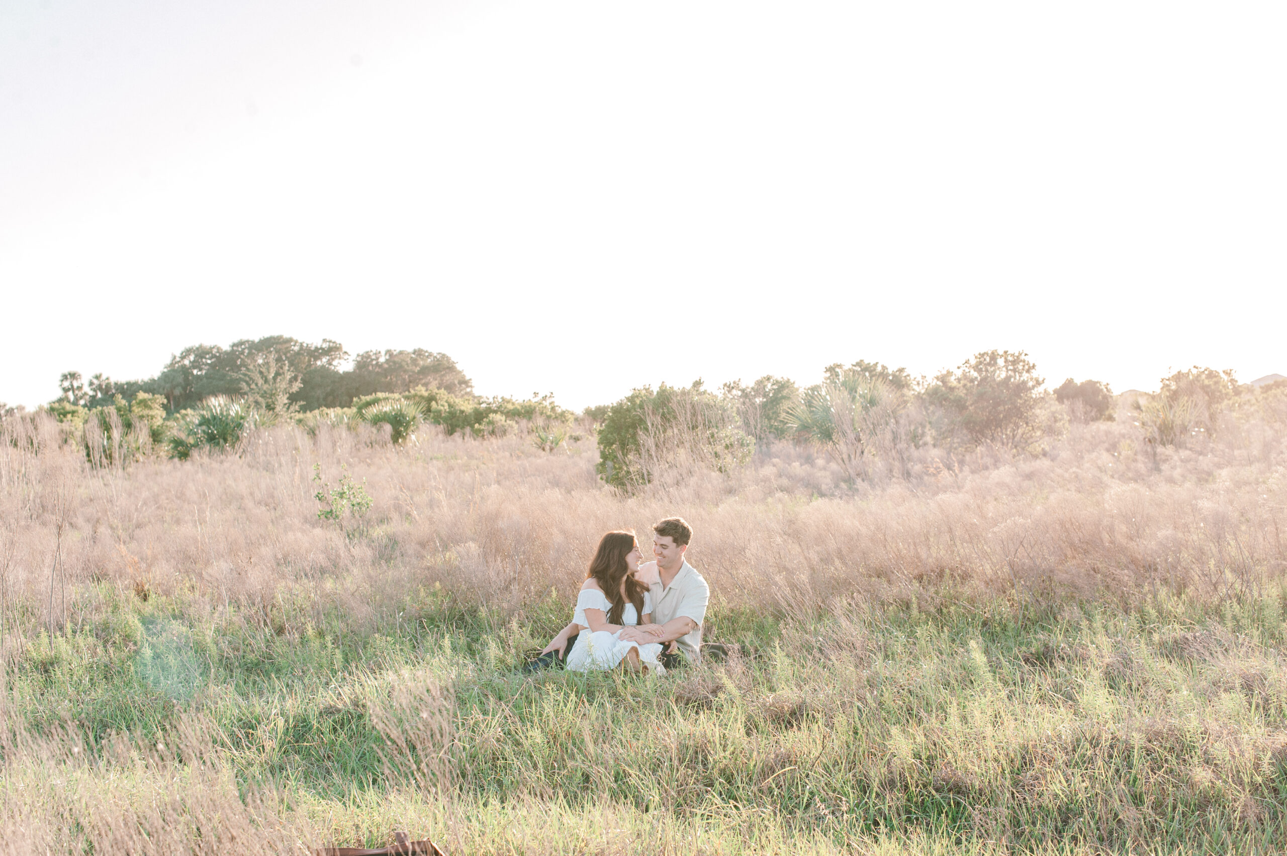 Couple in Central Florida, cozied up sitting in a tall grass field talking away about their future. 