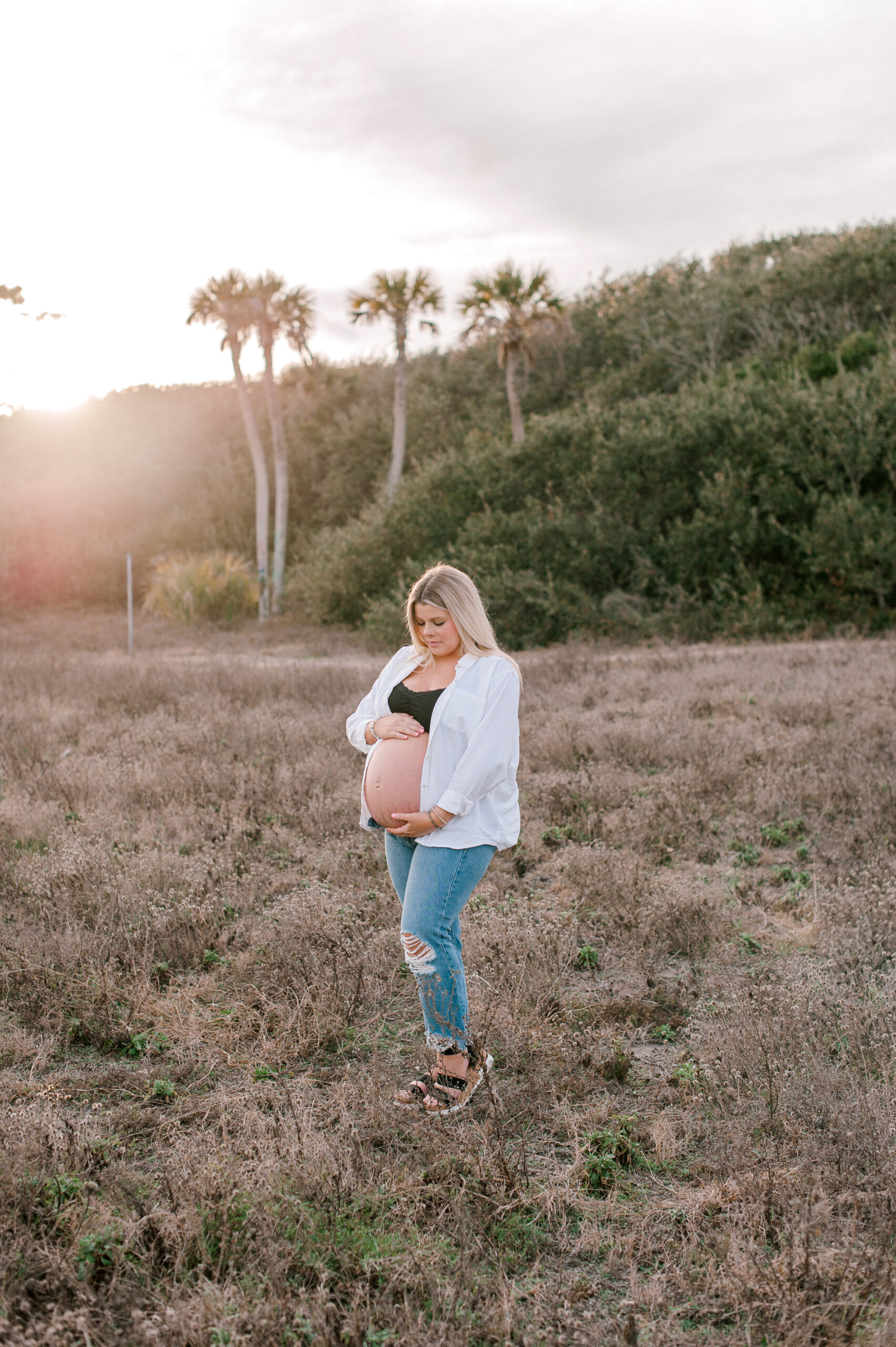 IVF mama holding her belly reflecting on her pregnancy journey at sunset in a field. 