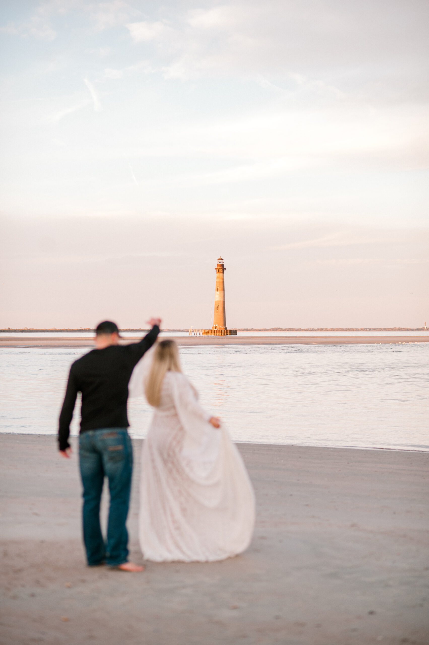 Photo of a lighthouse on the water at sunset with new parents blurred in the photo thinking of Reflections OBGYN. 