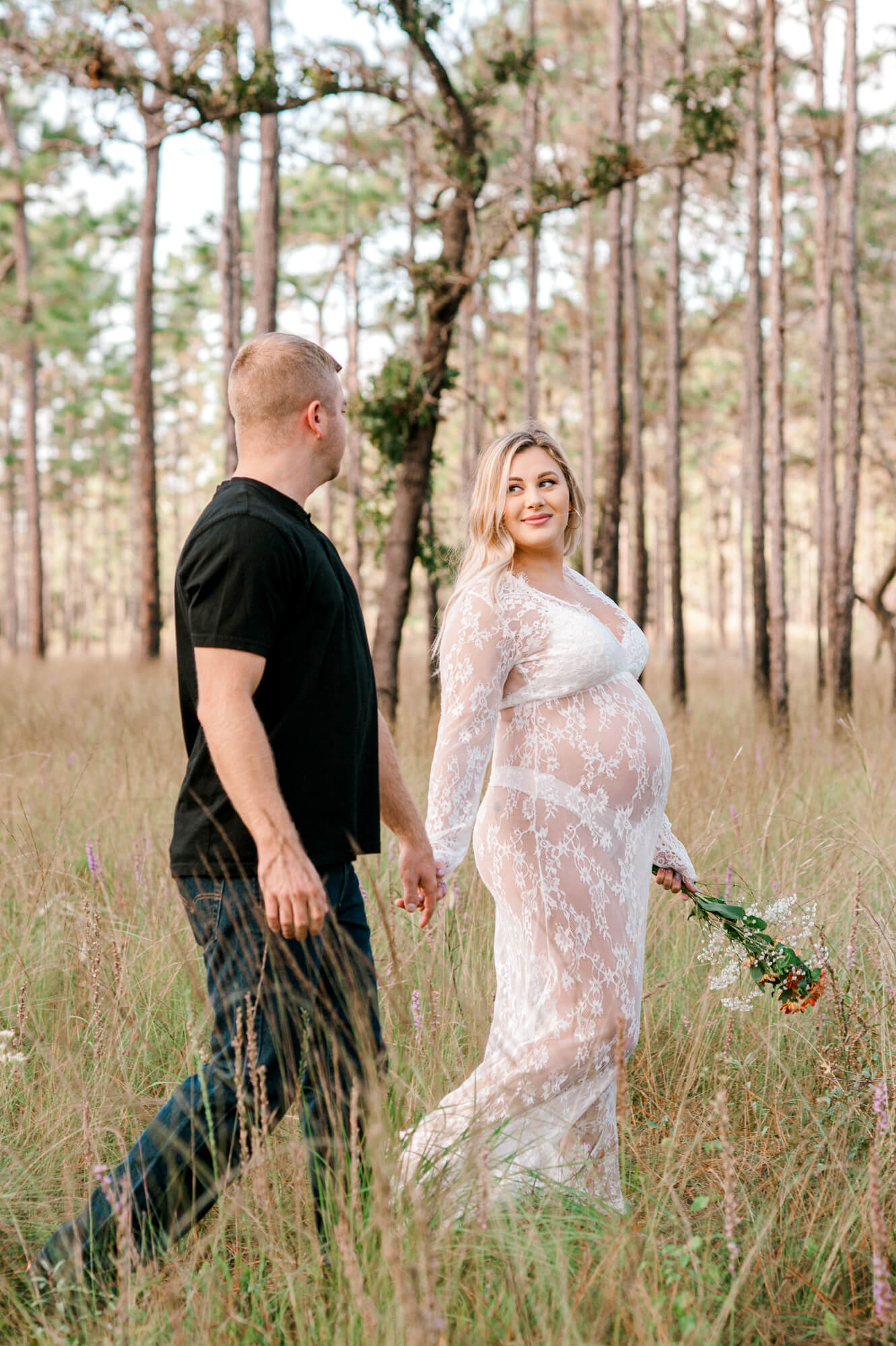 Stunning soon to be new parents walk through the tall grass hand in hand.
