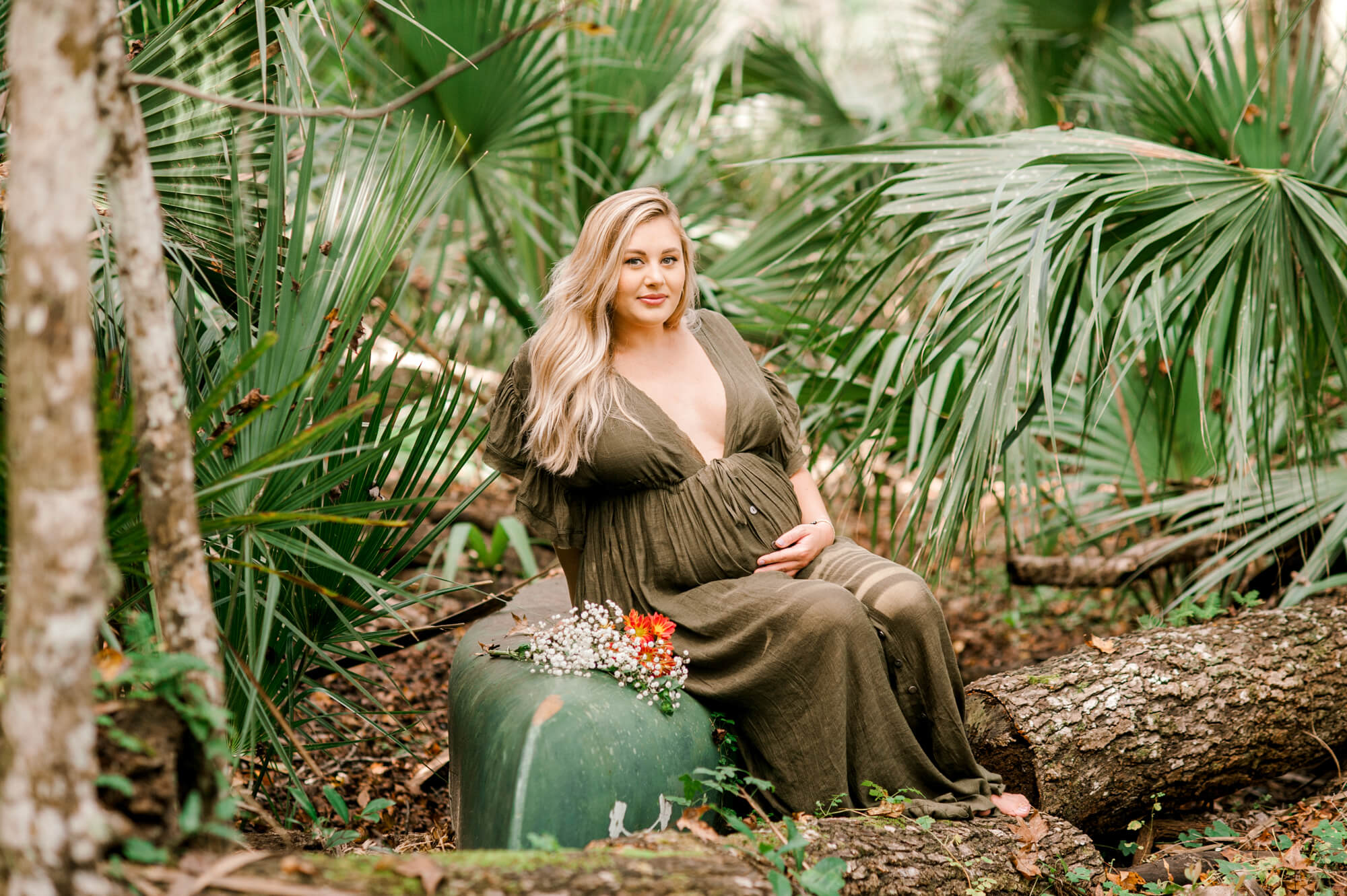 Beautiful new mom to be sits on a kayak with flowers during her maternity session at an Orlando Spring.