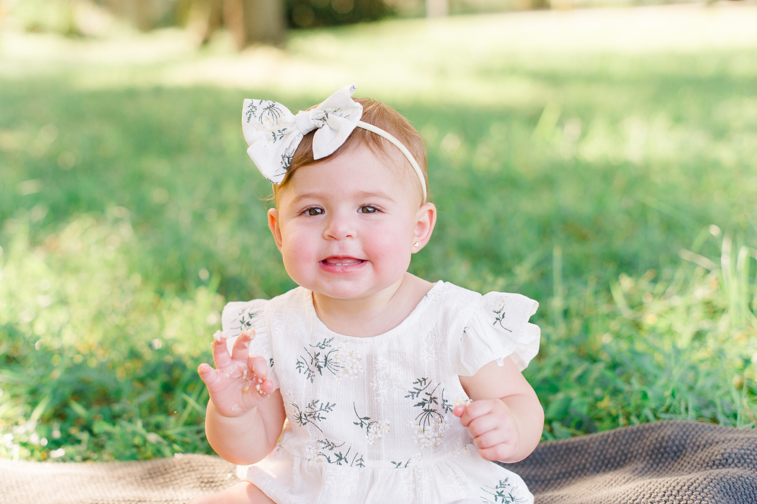 Adorable milestone session of a little girl sitting on a blanket in the grass clapping!