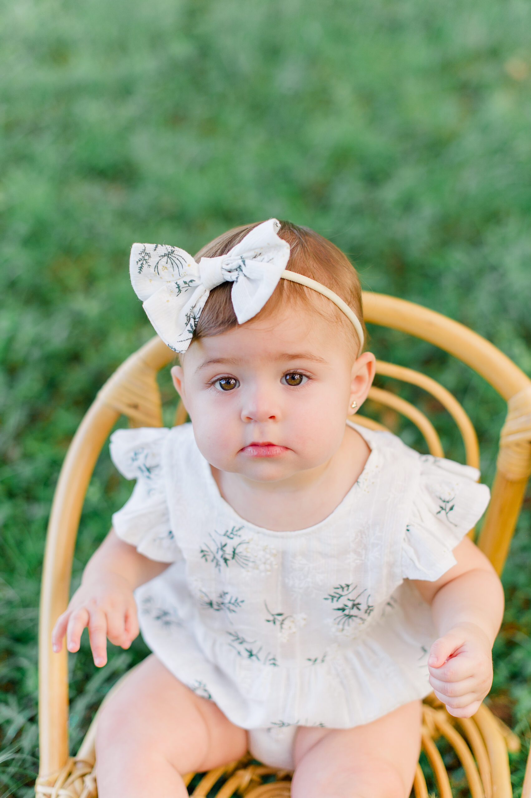 Closeup of a young girl sitting in a wicker chair in the grass during her milestone session