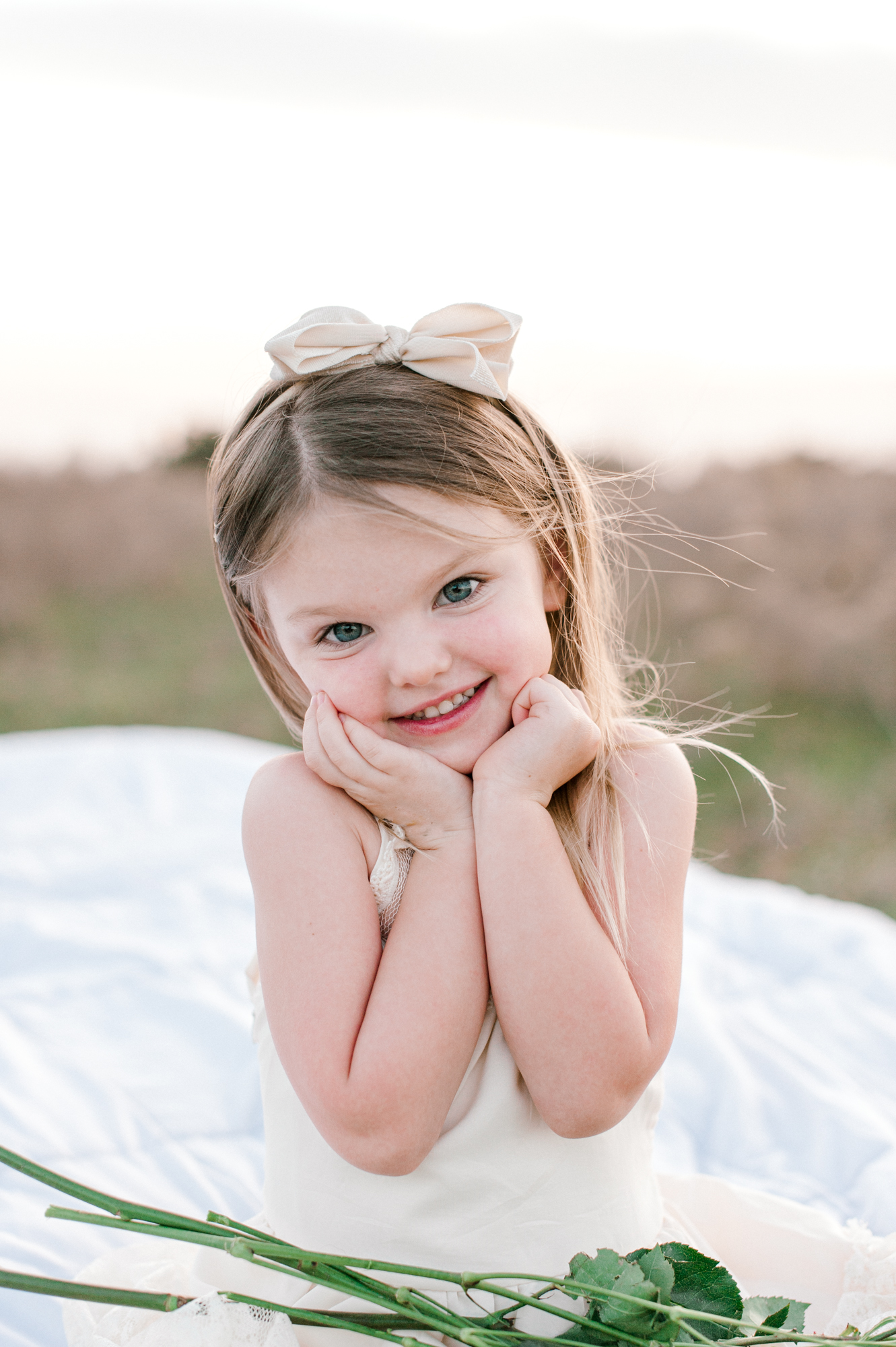 Toddler girl holdign her cheeks and smiling into the camera at sunset during her photoshoot. 