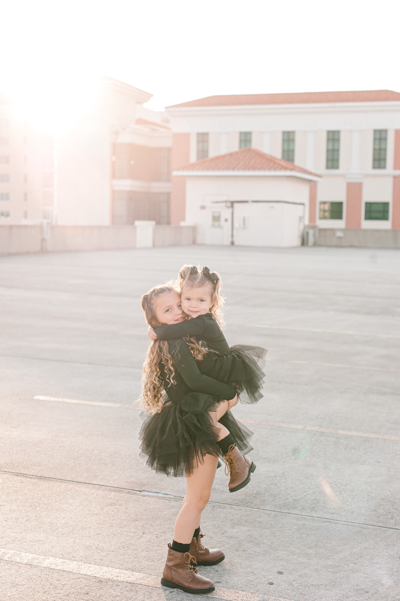 Sisters loving each other with a huge hug in the cutest black tutus on top of a parking garage at sunset.