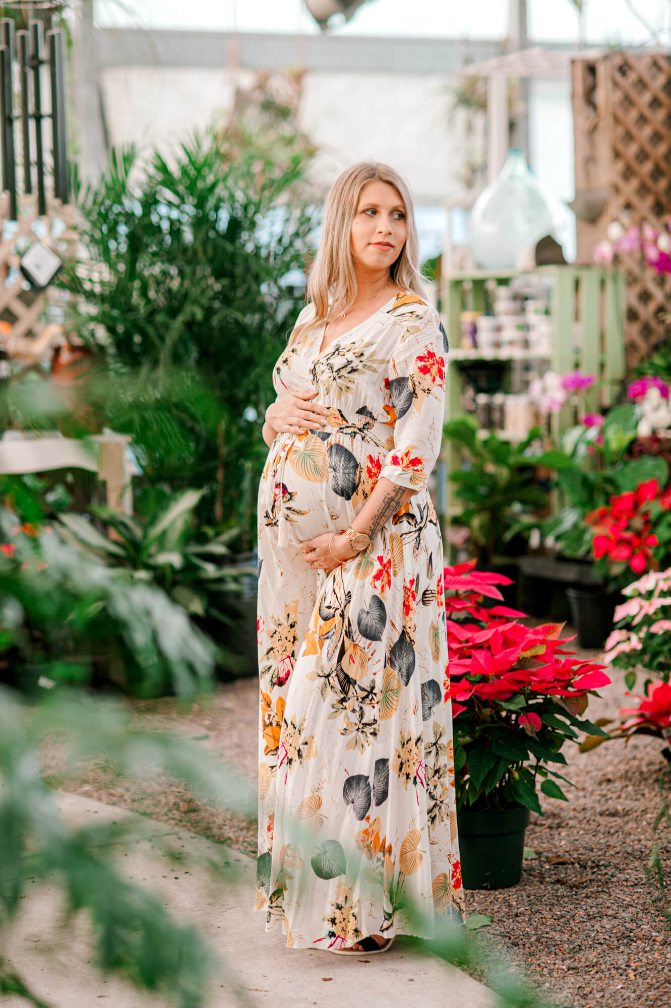 Mom standing in a green house looking over her shoulder while holding her belly with both hands.