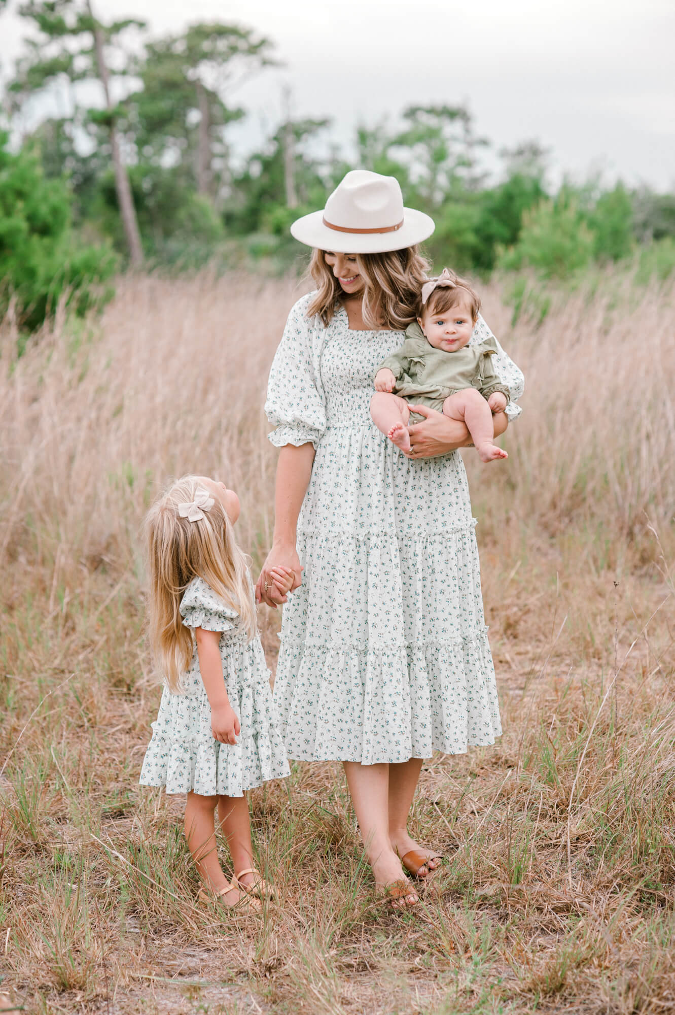 Mom standing in a field in Viera, Florida holding her baby and her older daughters hand.
