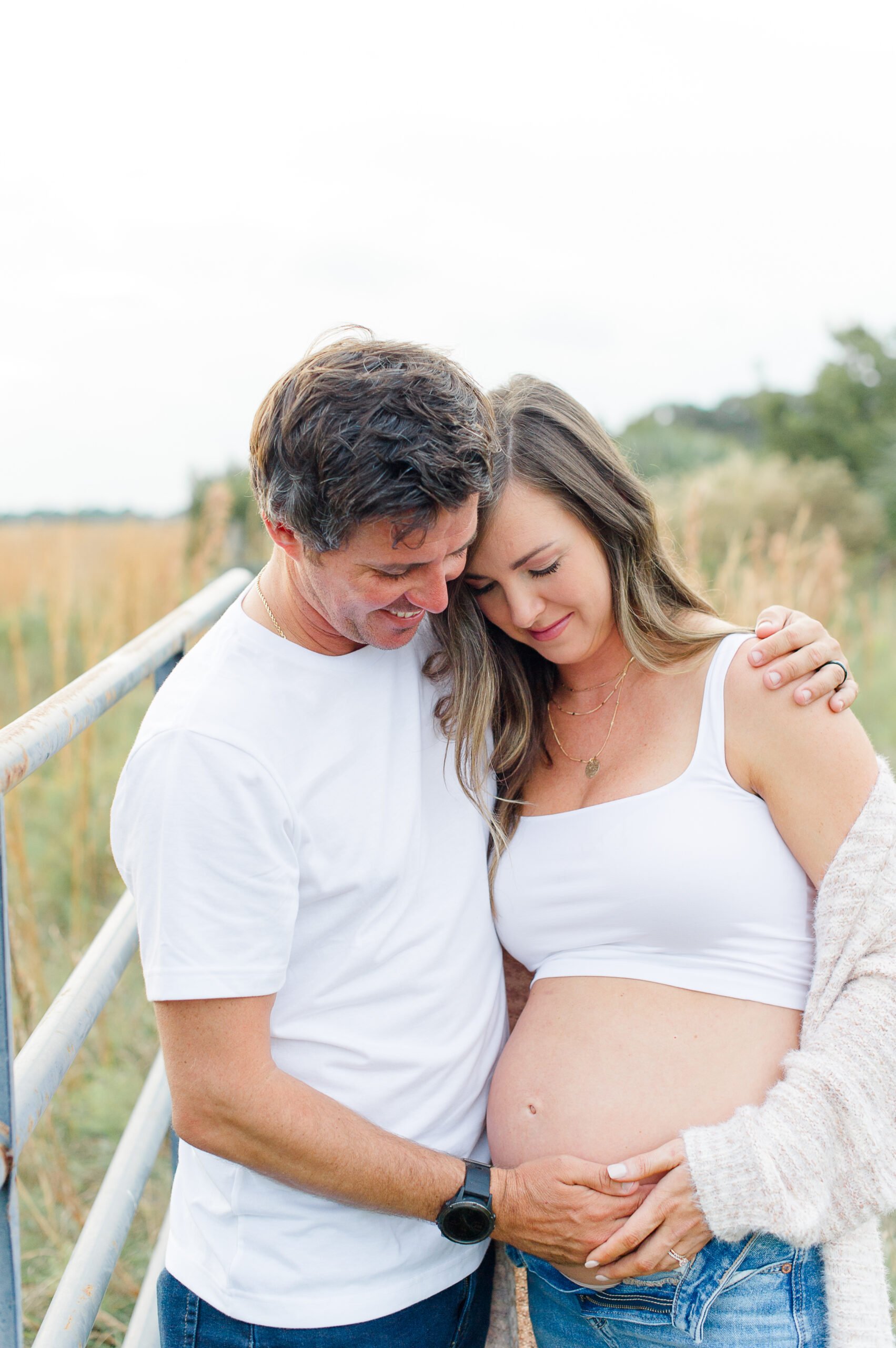 New parents hugging while holding moms pregnant belly in a tall grass field