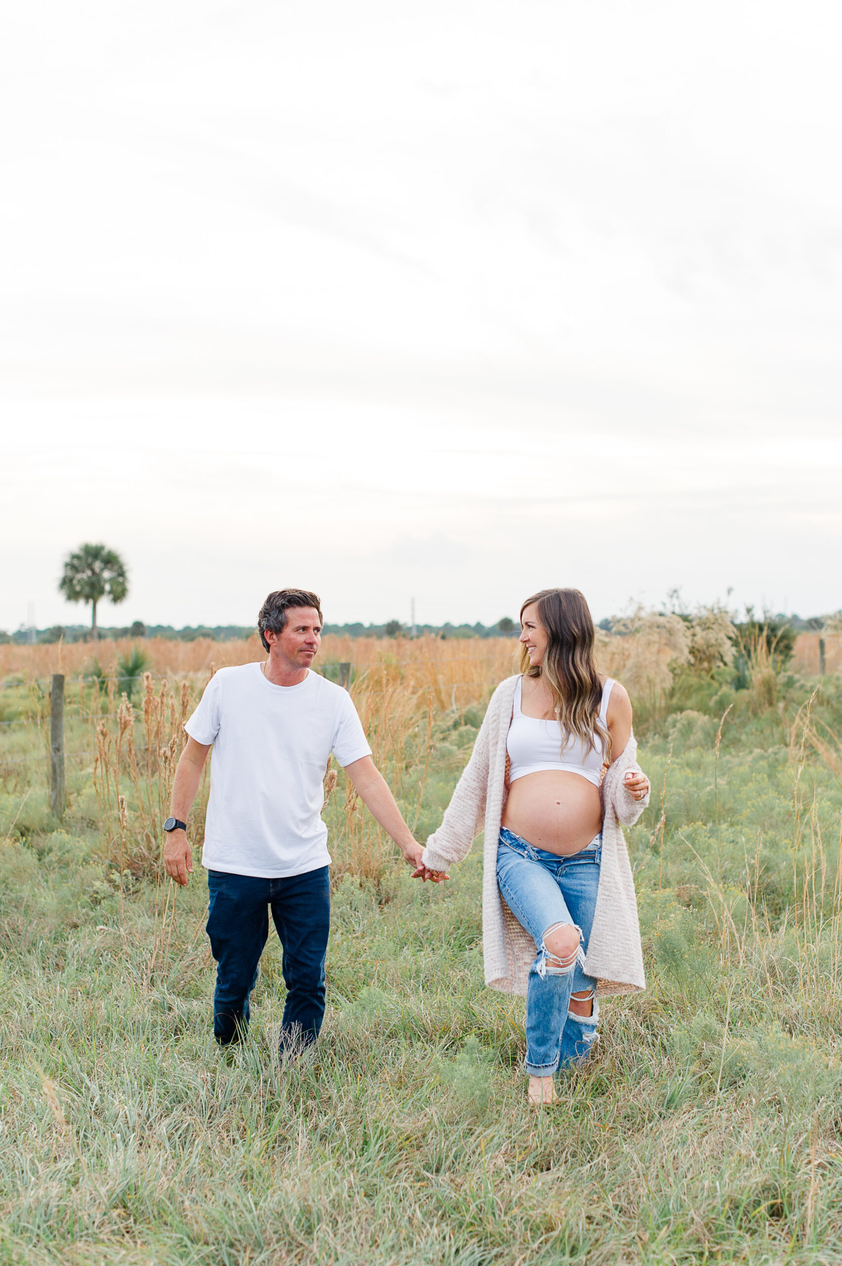 The cutest soon to be new parents to a sweet babygirl, walking through a field of tall grass at sunset
