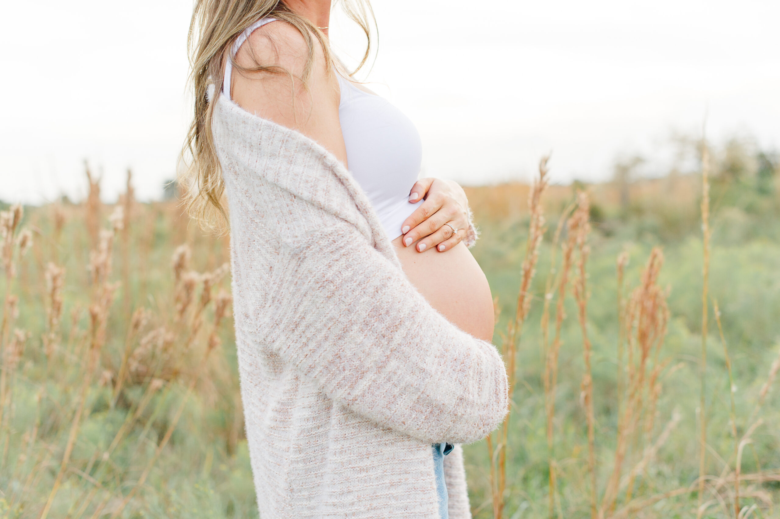 Expectant mother holding her belly in a tall grass field during sunset maternity photos Orlando Birth Center