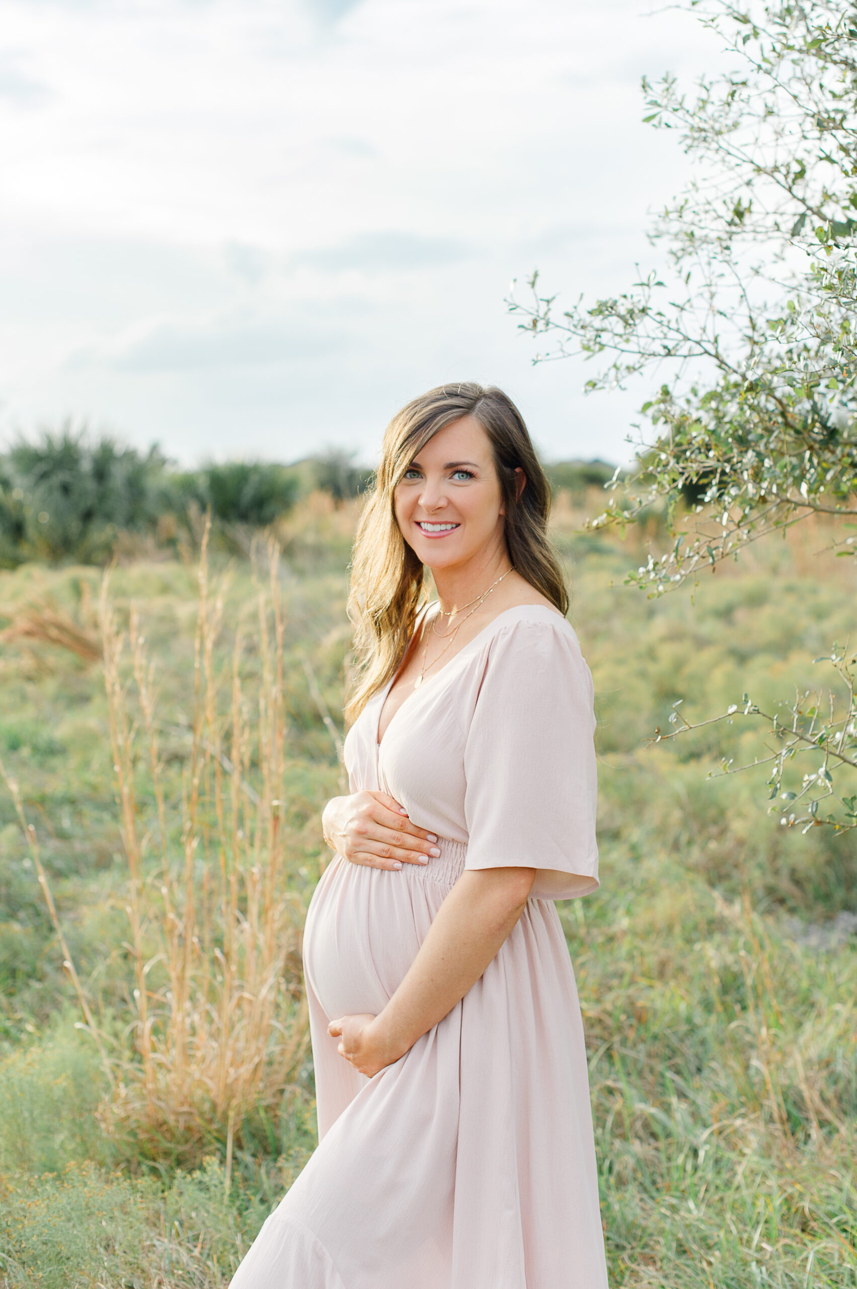 New mother standing in a field of tall grass holding her bump Orlando Birth Center