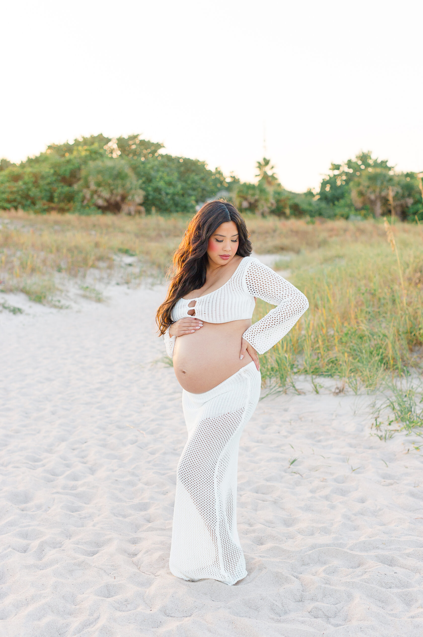 Stunning image of a pregnant mother standing on the beach near the dunes at sunset Orlando Doulas