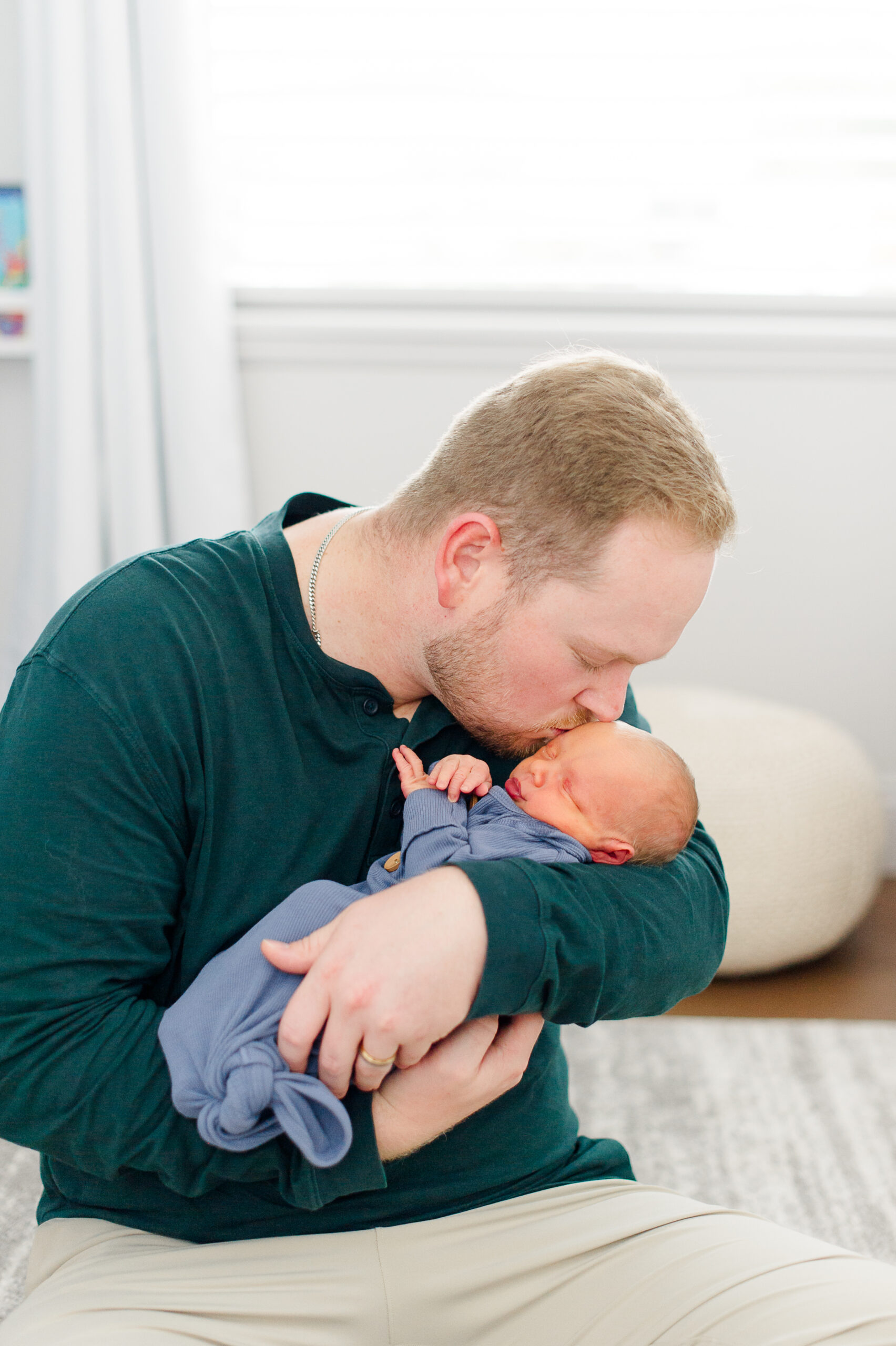 Dad holds newborn son close and gives him kisses on the forehead during newborn photos.