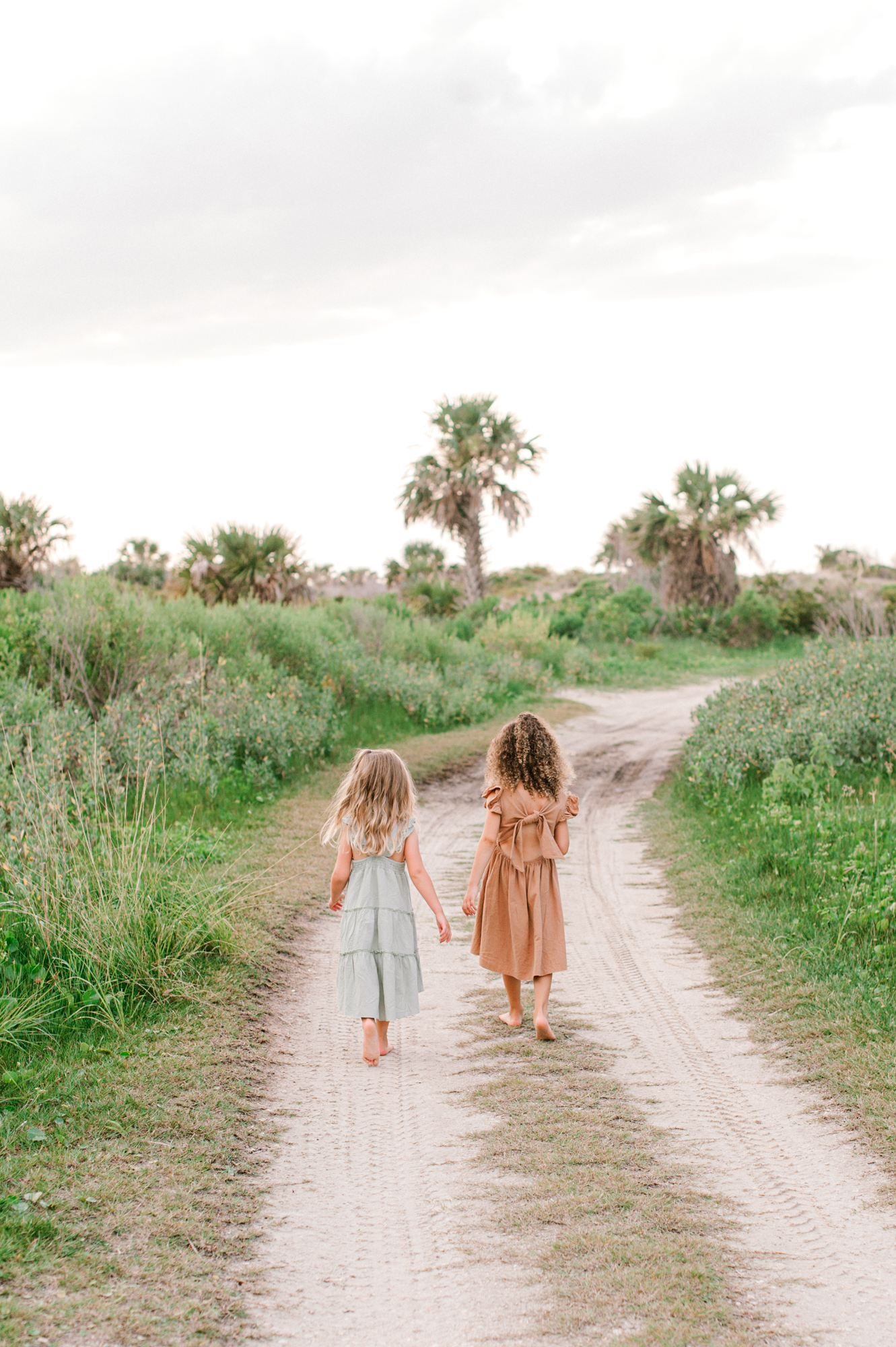 Sisters walking down a path toward the beach holding hands at sunset Orlando pediatricians 