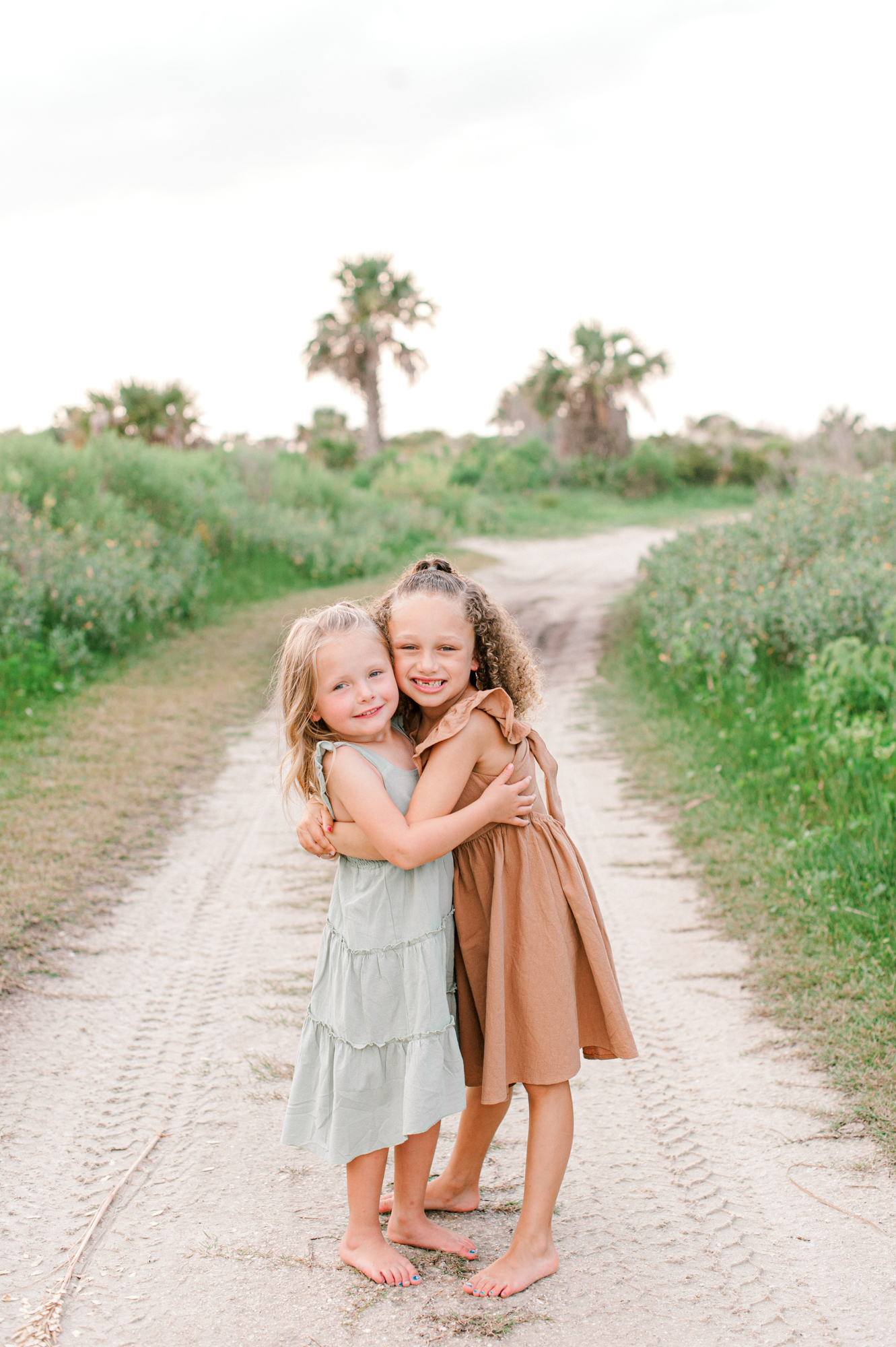 Sweet sisters standing on a beach access path hugging and smiling at the camera
