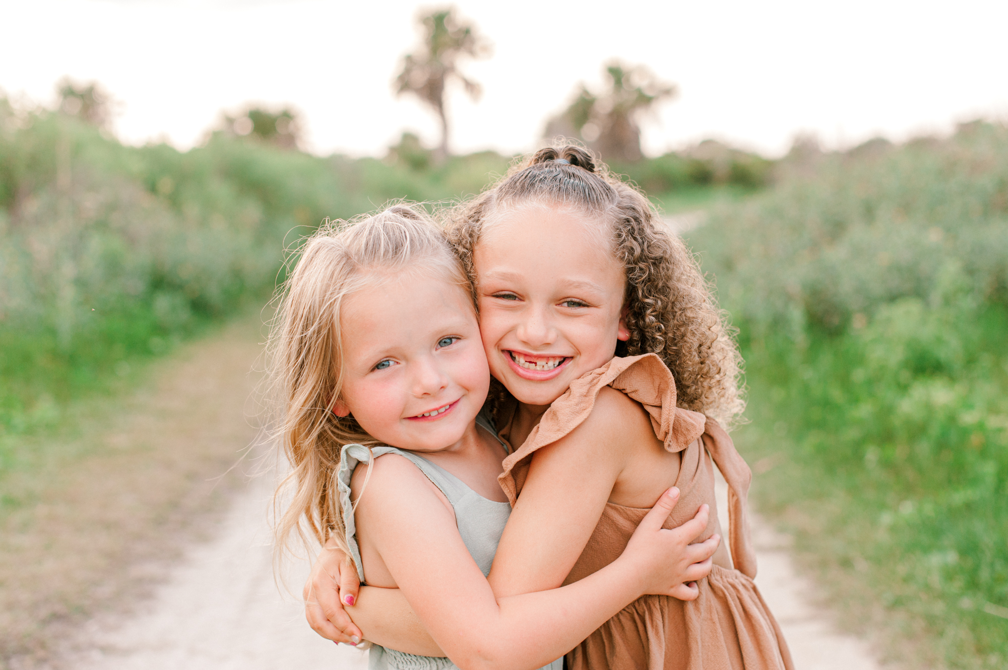 Two adorable sisters hugging each other tight and smiling at the camera during their family photoshoot at sunset Orlando pediatricians