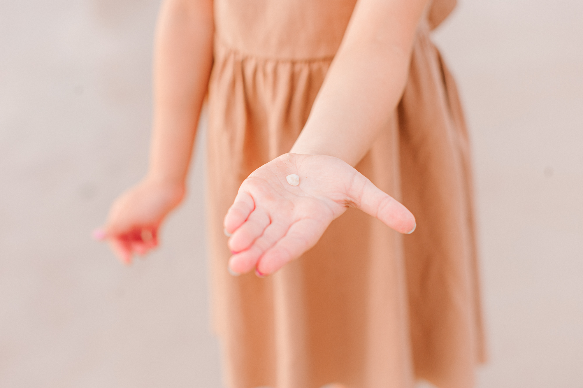 Young daughter holding a tiny seashell she found at the ocean during their family photoshoot
