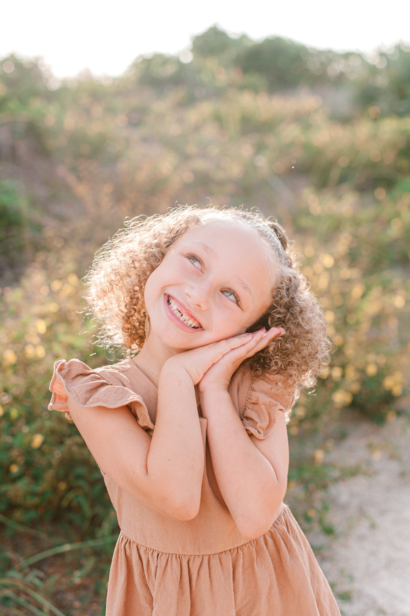 Adorable close-up of a little girl smiling with her hands on her cheek smiling up a the sky