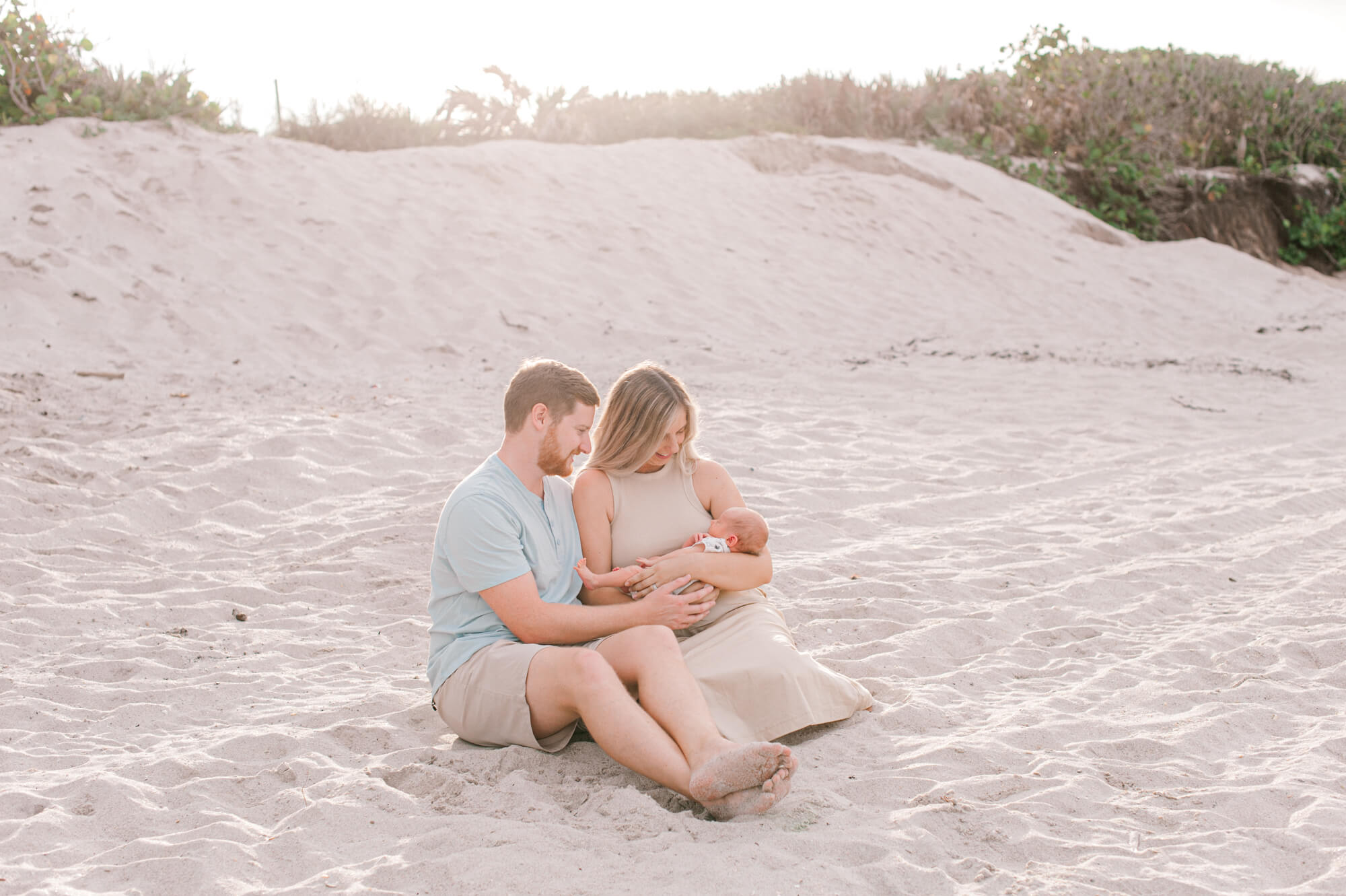 New parents sit on the beach with their sweet new baby boy during their Newborn Family Photographer session and hold him close at sunset Orlando baby stores