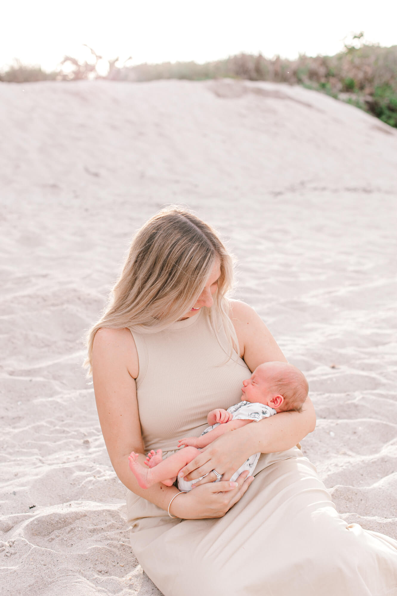 New young mom sits near the dunes on the beach at sunset holding her sweet new bundle of joy, her newborn baby boy Orlando baby stores