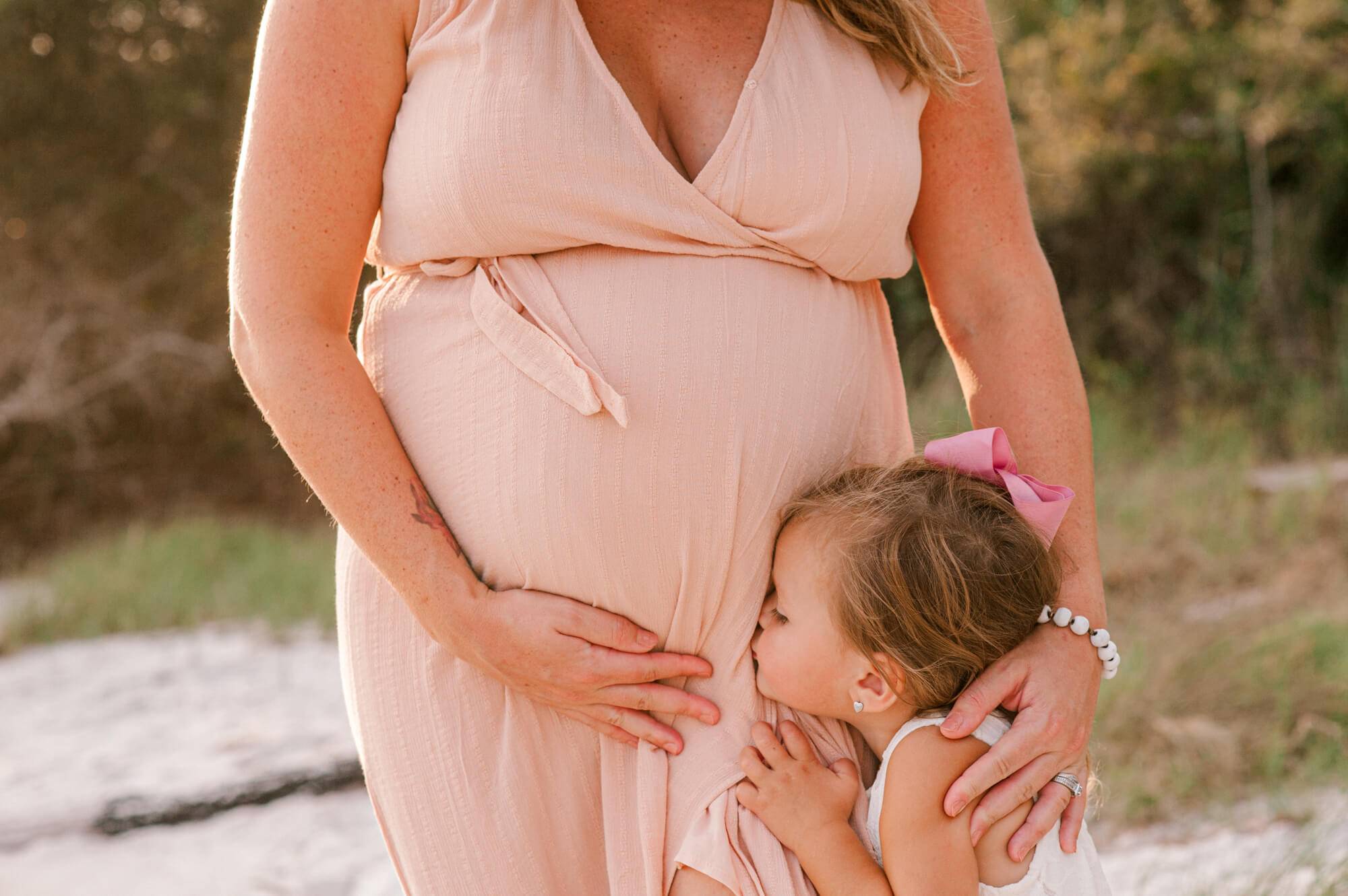 little girl kissing moms pregnant belly on the beach at sunset orlando birth center