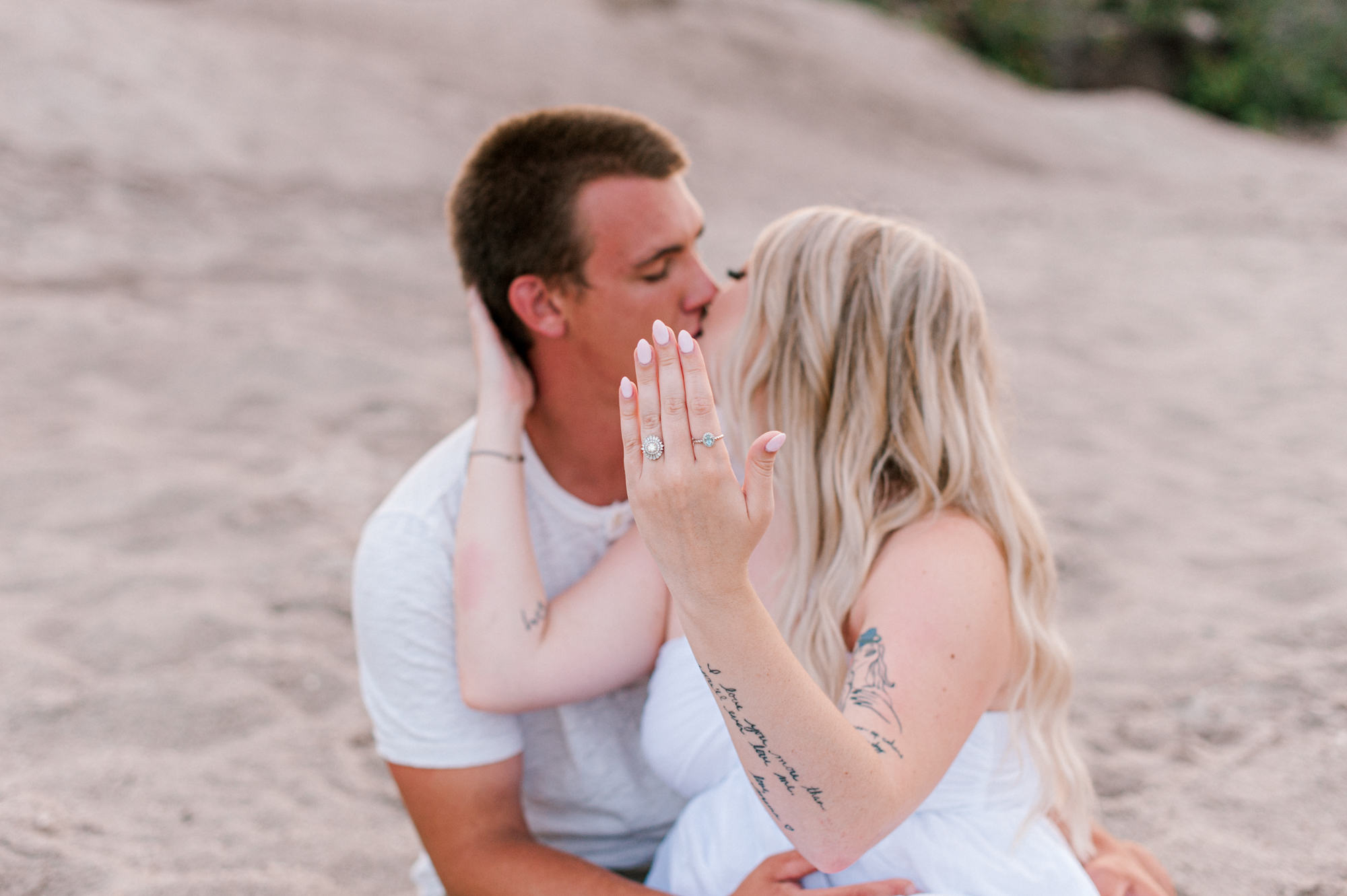 Couple kissing near the dunes while the young girl shows off her engagement ring during their photoshoot on the beach