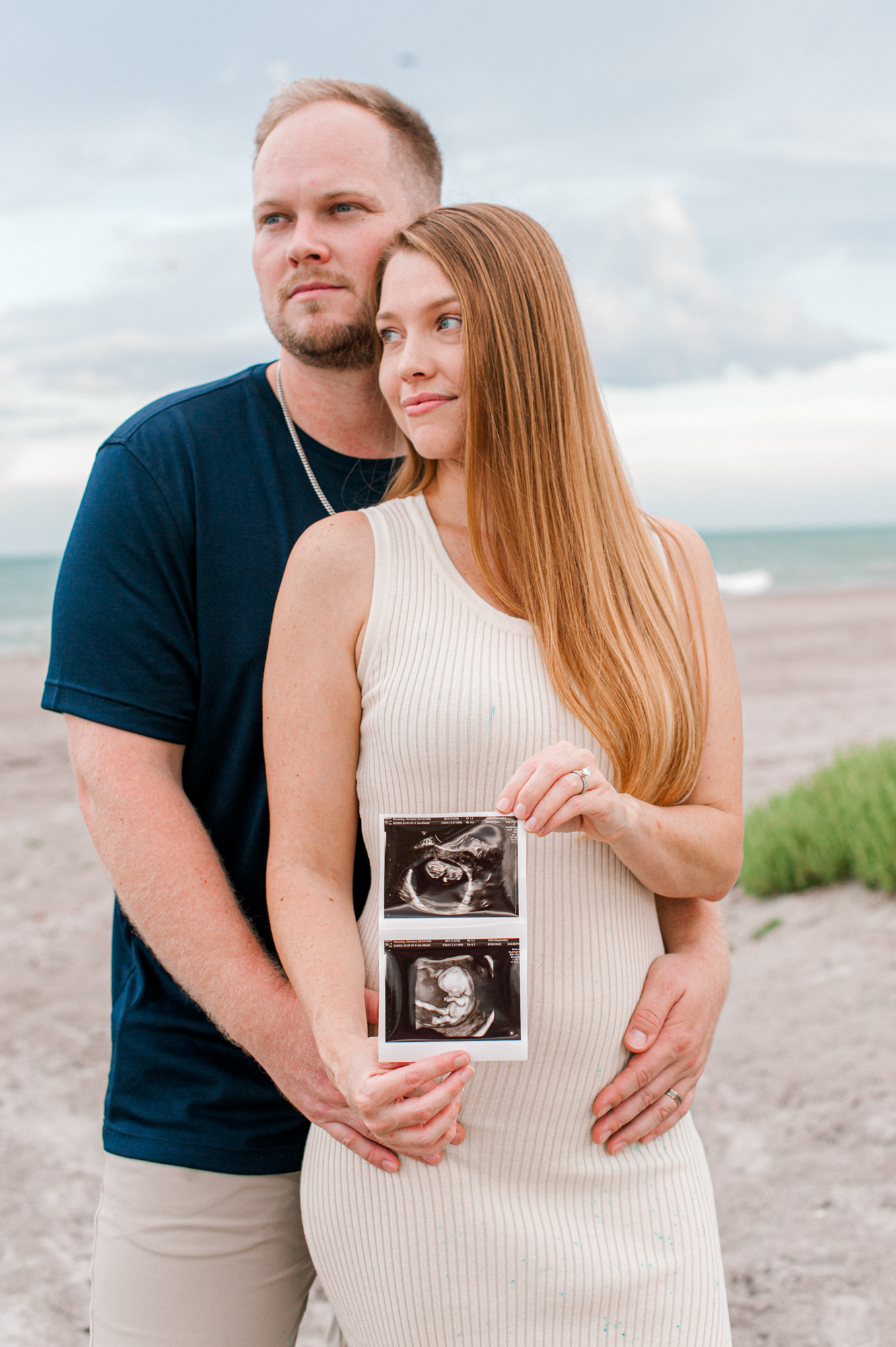 New parents hold an ultrasound photo over moms pregnant belly at the beach during their announcement photoshoot