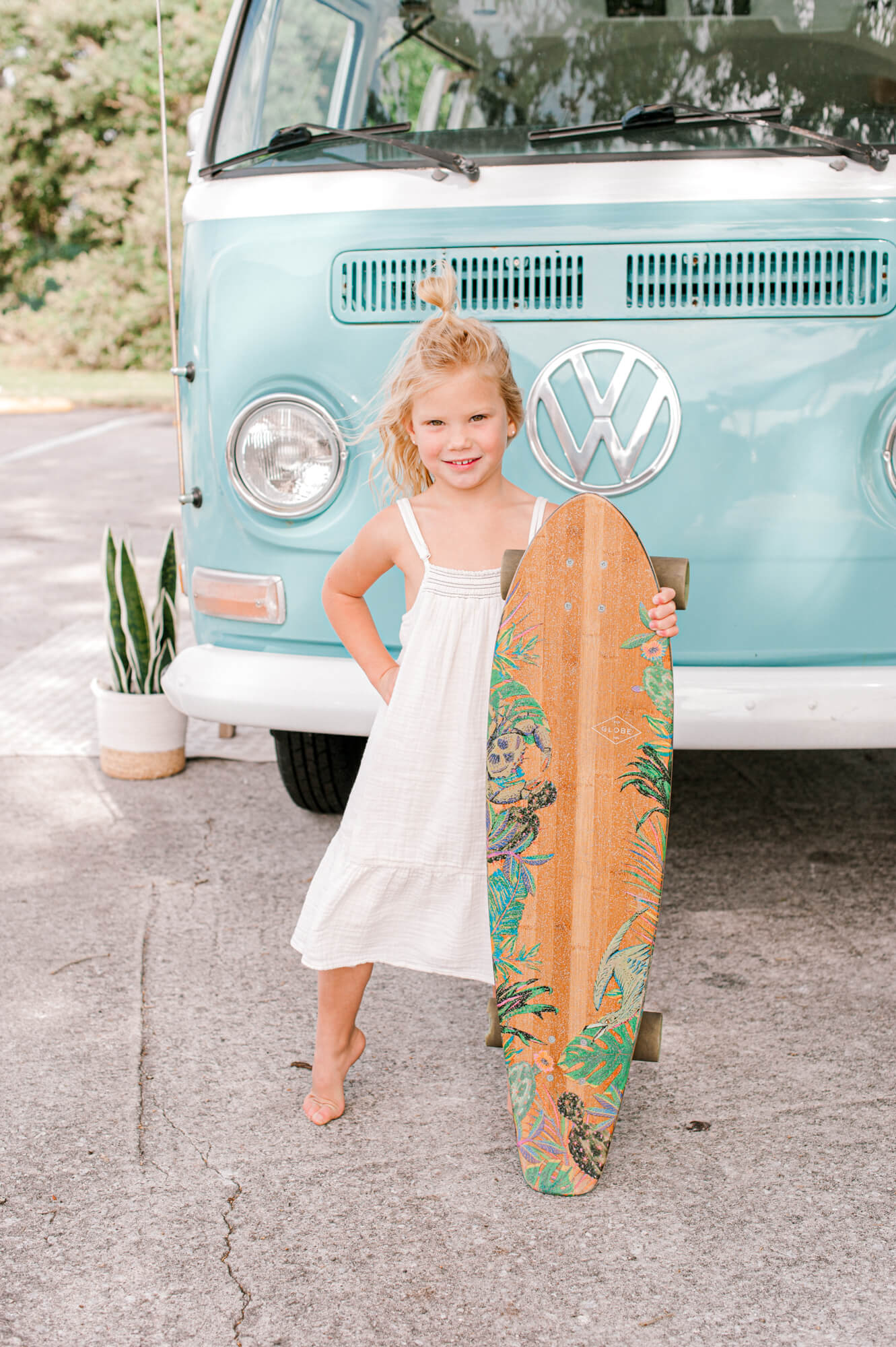 Cutest young blonde beach babe holding a skateboard and posing in front of a VW bus