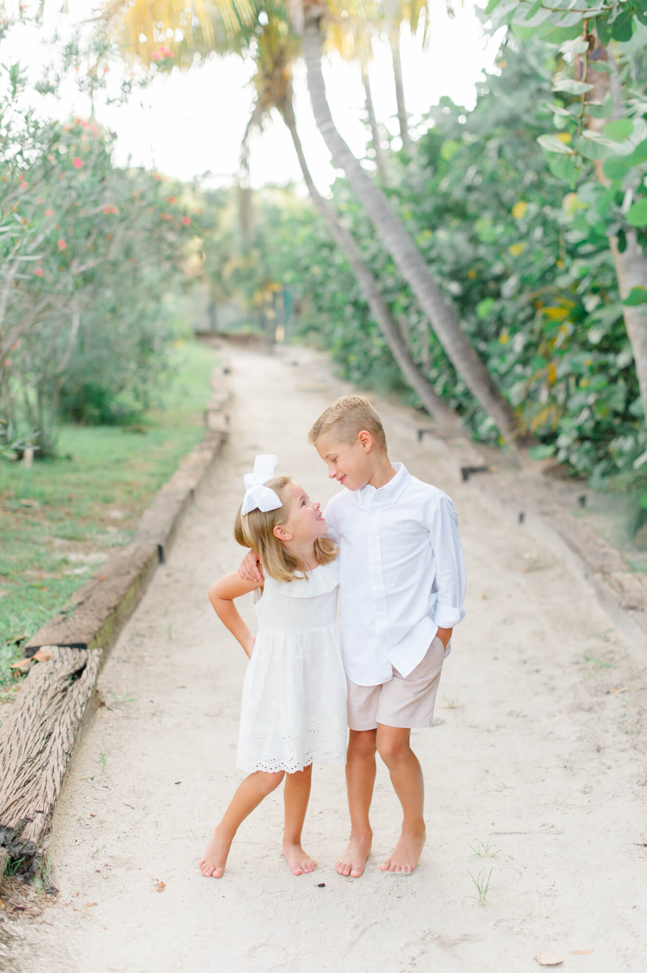 Sweet siblings smiling at each other on the beach path with beautiful greenery and palm trees all around