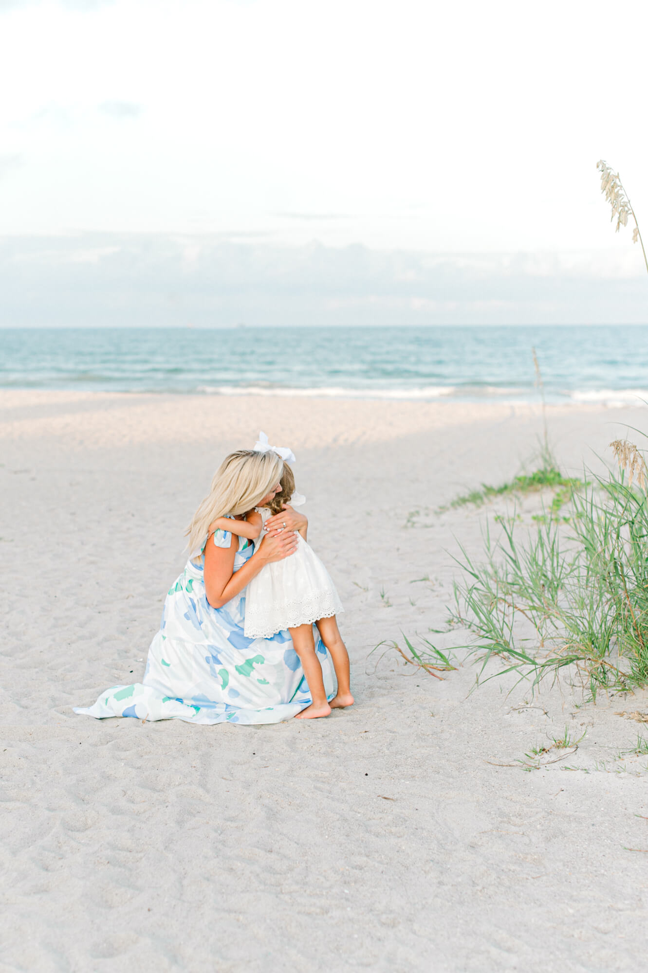 Mom hugging her daughter near the dunes with the beautiful beach landscape in the background