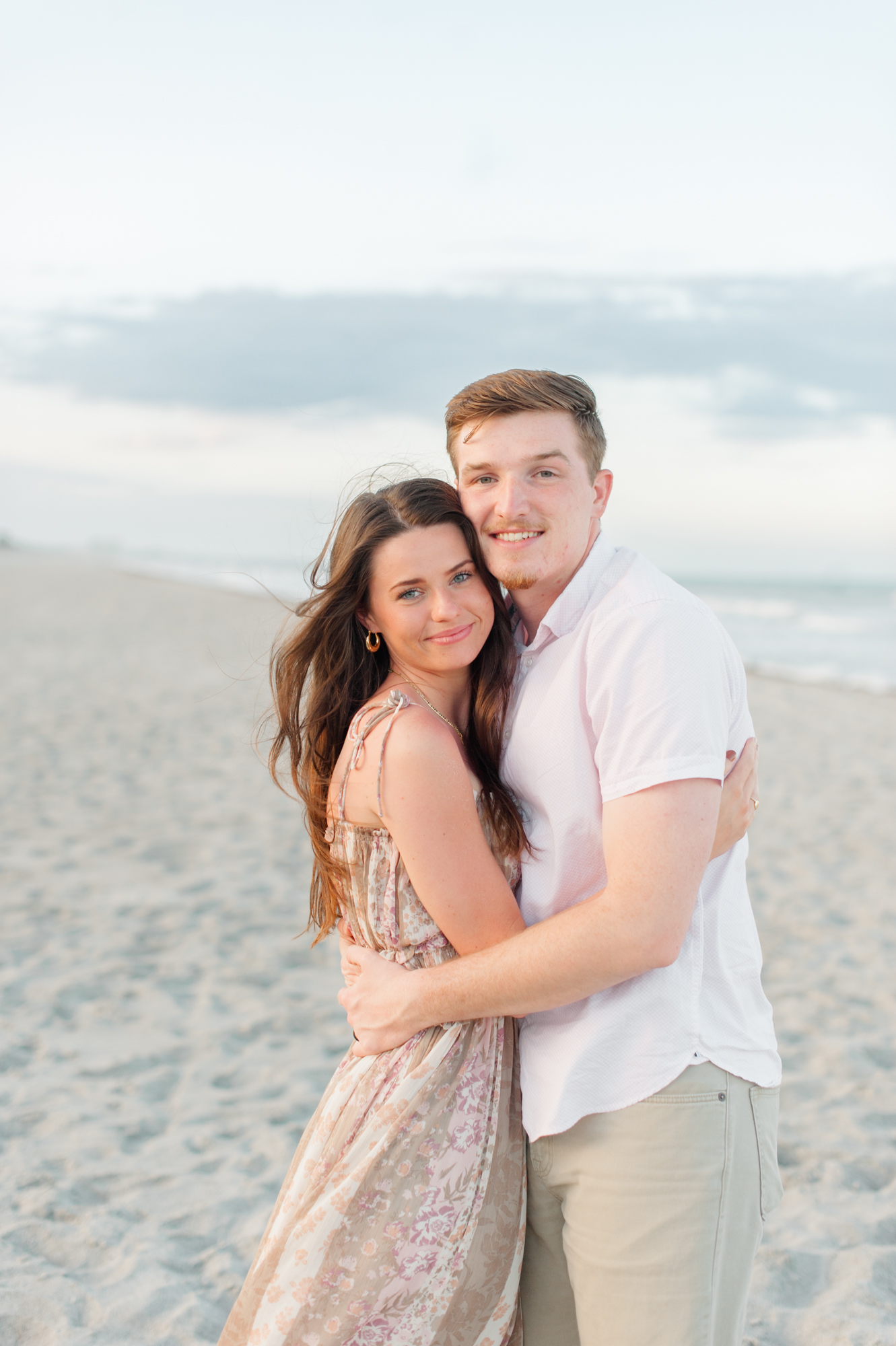 Sweet, stunning young couple poses at the beach and smiles holding each other dearly during their sunset photoshoot Orlando yoga studios