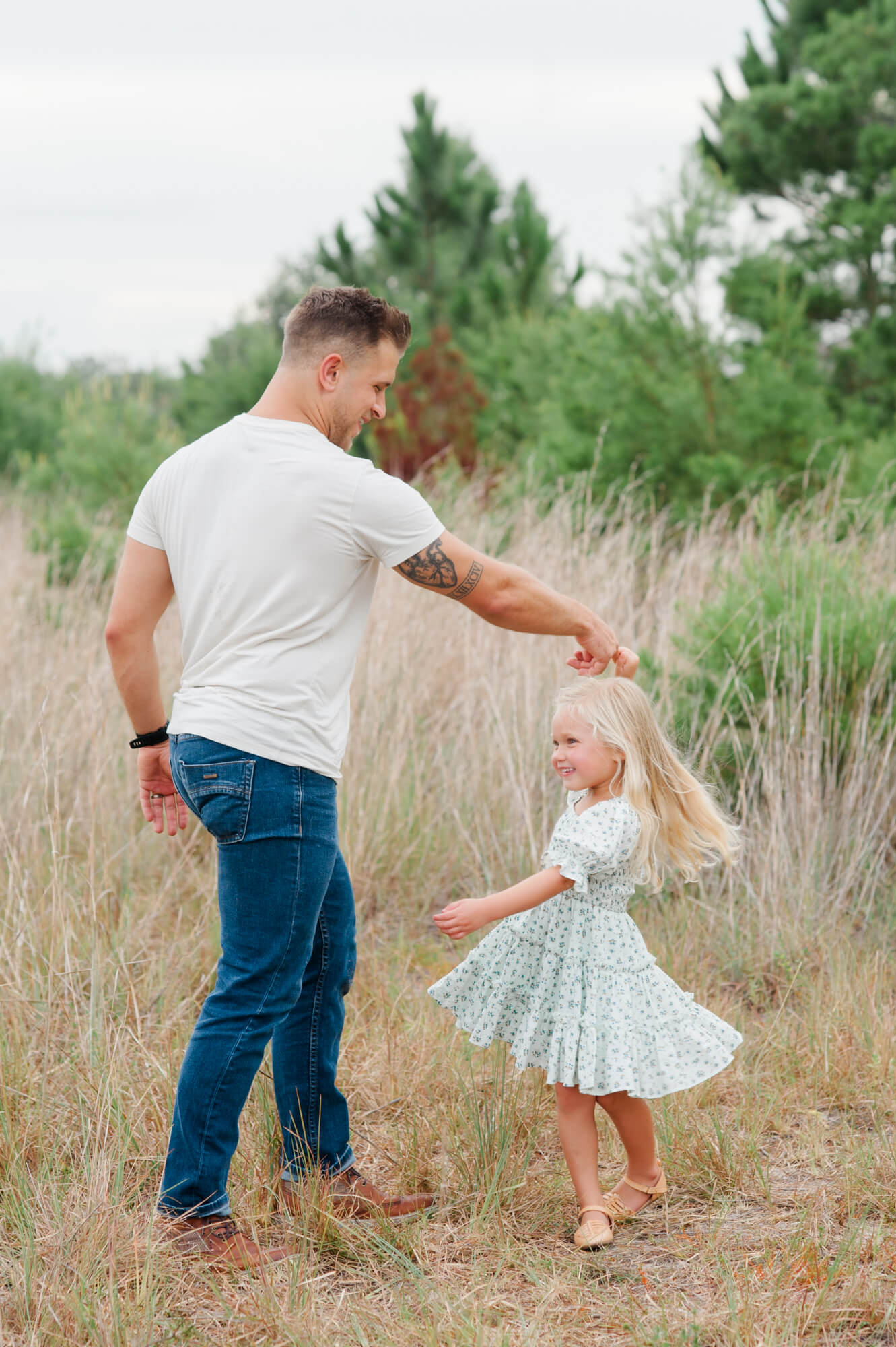 Dad dancing and twirling daughter in a tall grass field during their family session wearing greens and neutrals.