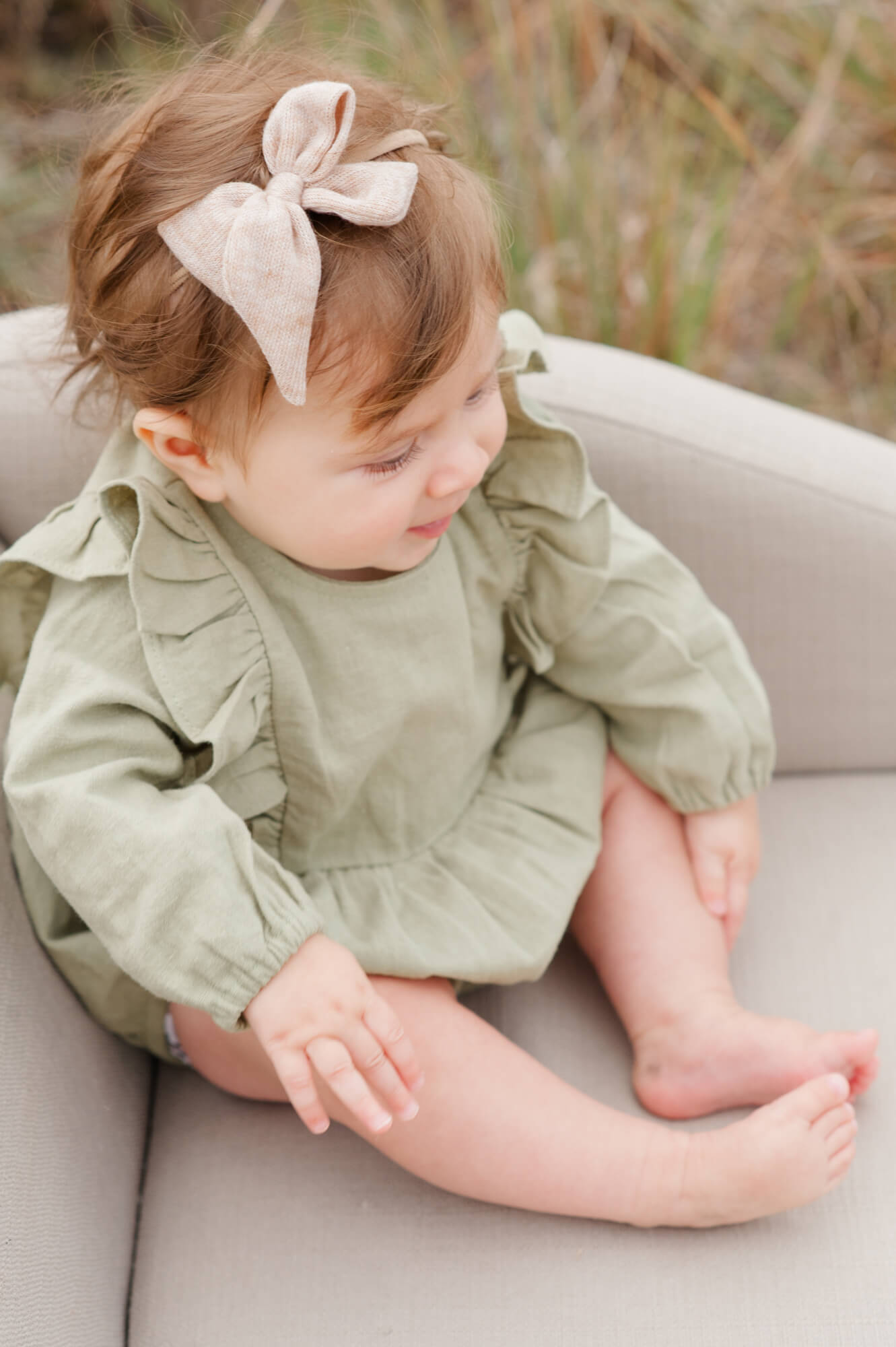 Closeup of young daughter wearing the cutest green romper with a bow sitting on a mini couch